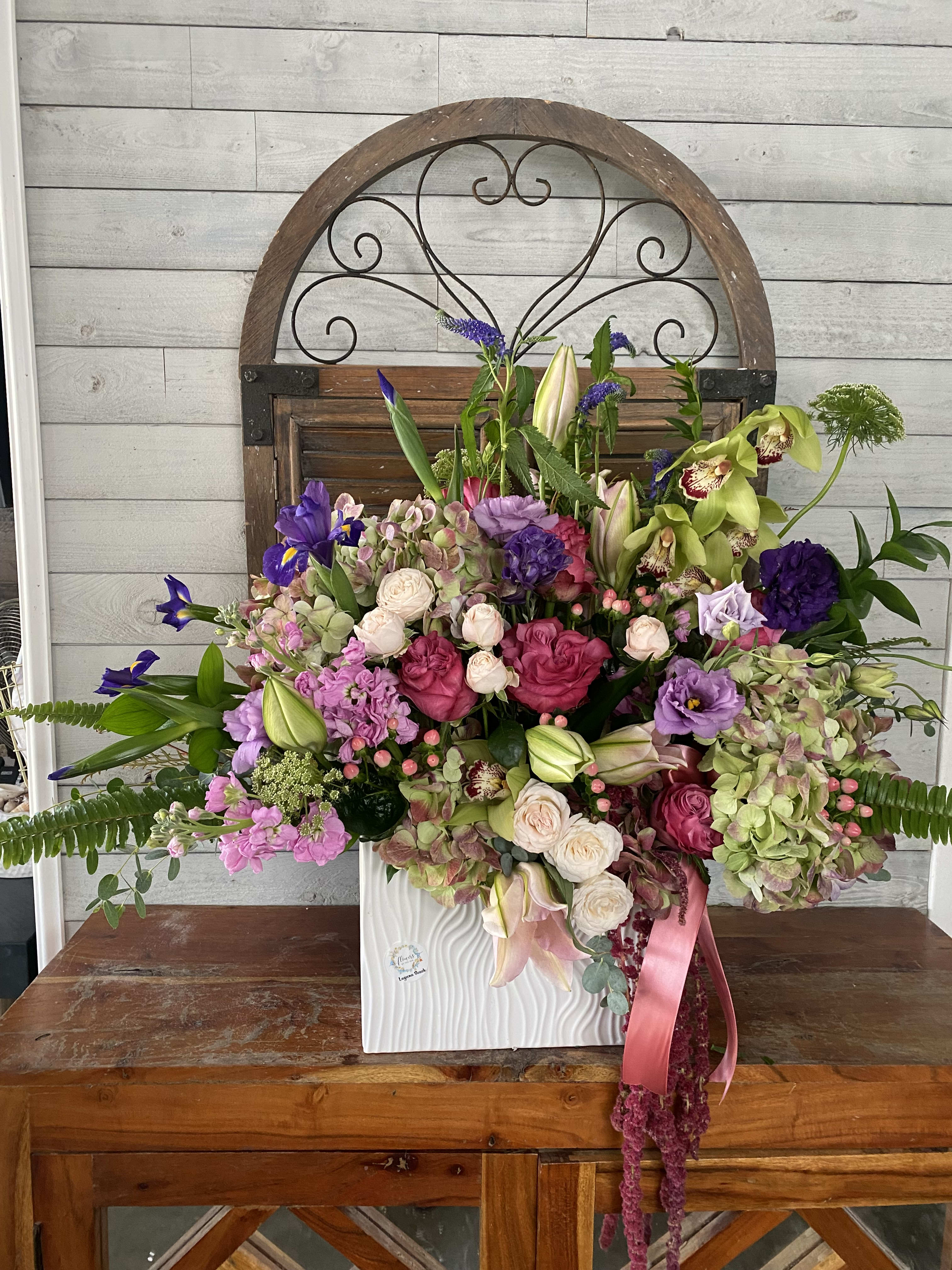 Large mixed floral arrangement in a white vase with pink ribbon