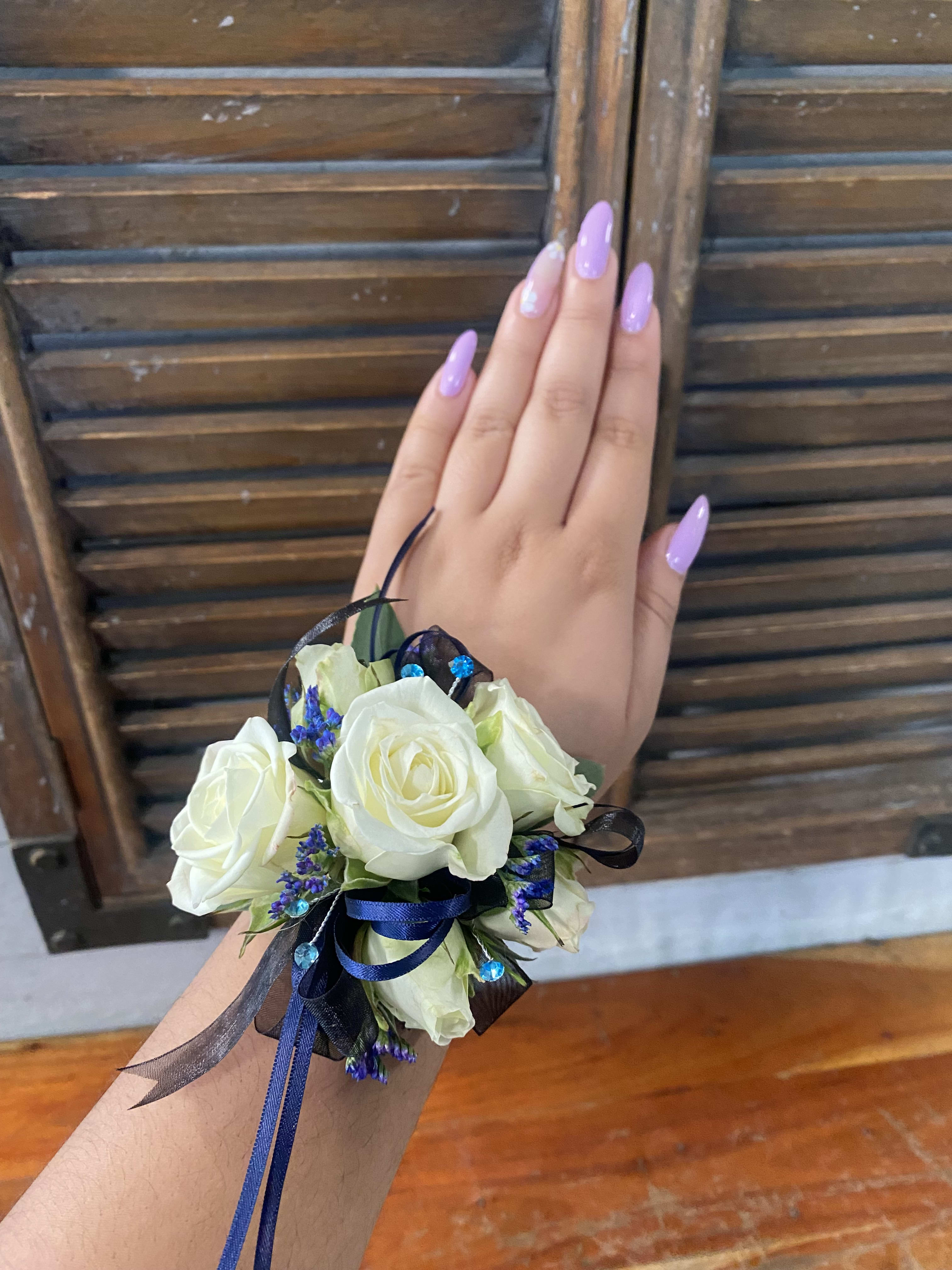 White rose wrist corsage with blue ribbon and small purple accents