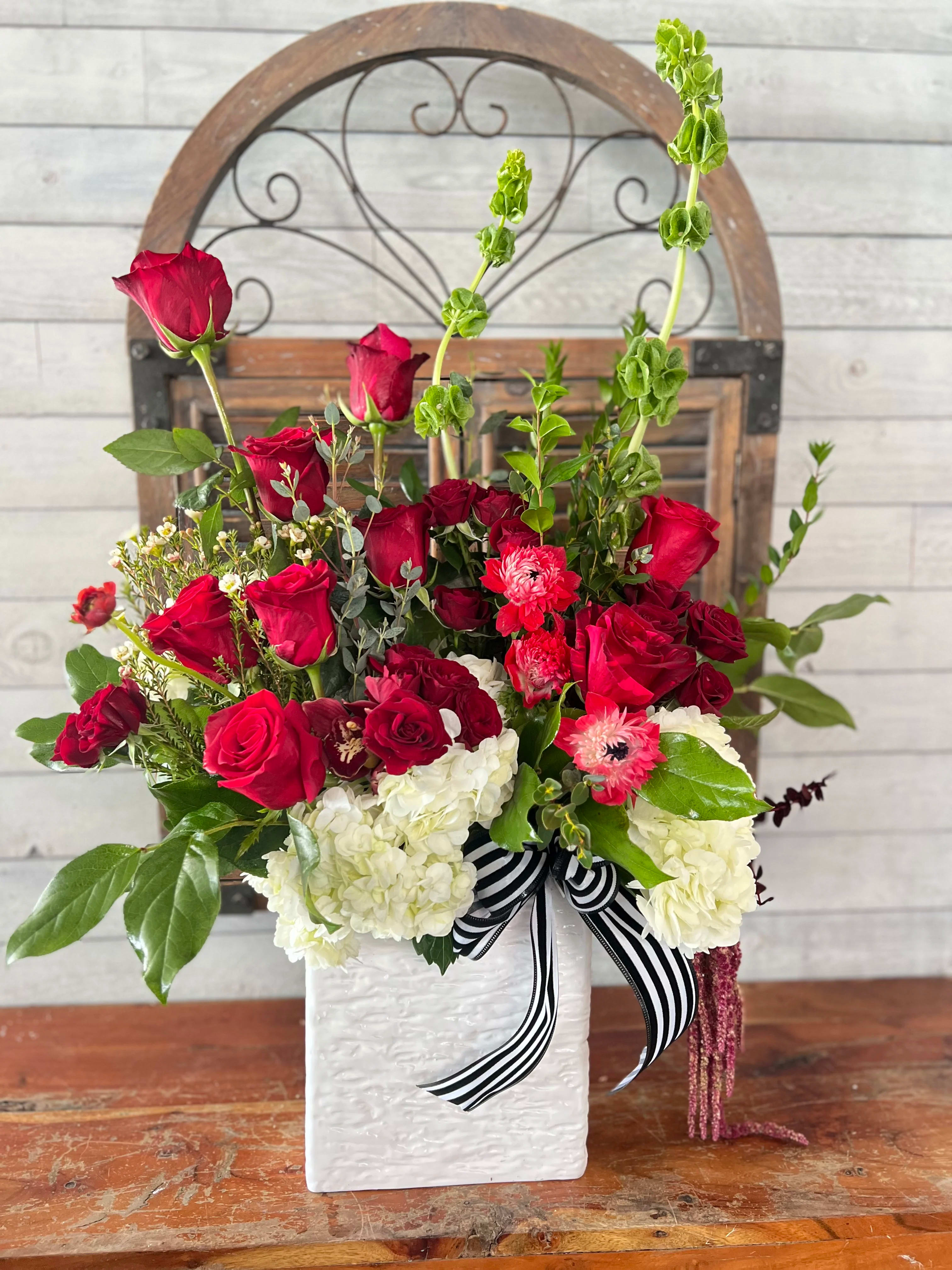 Red roses and white hydrangeas in a white vase with a striped ribbon