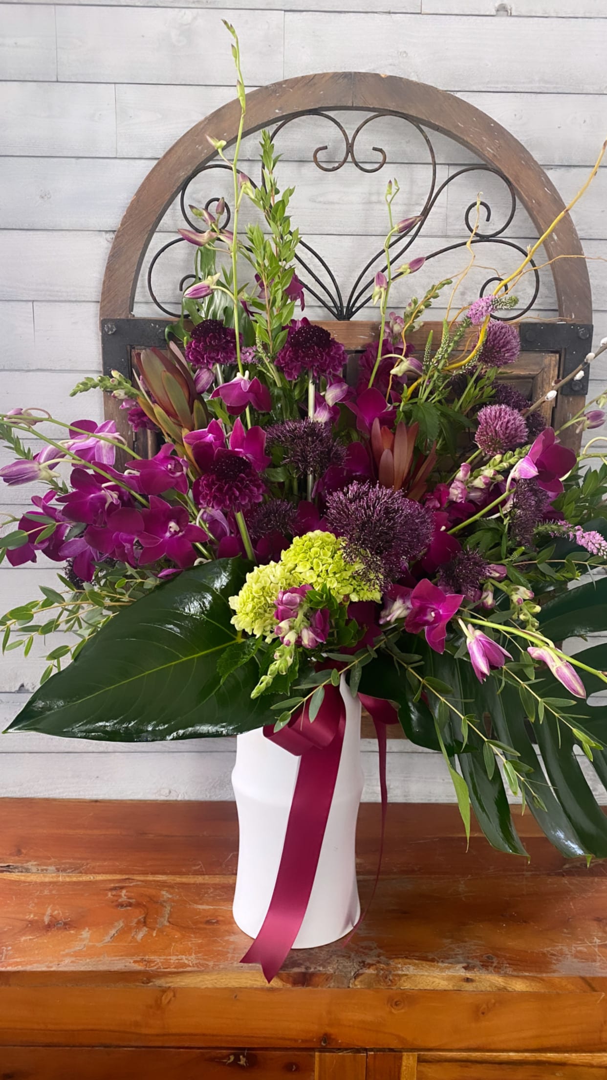 Tall magenta orchid arrangement in a white vase with a ribbon