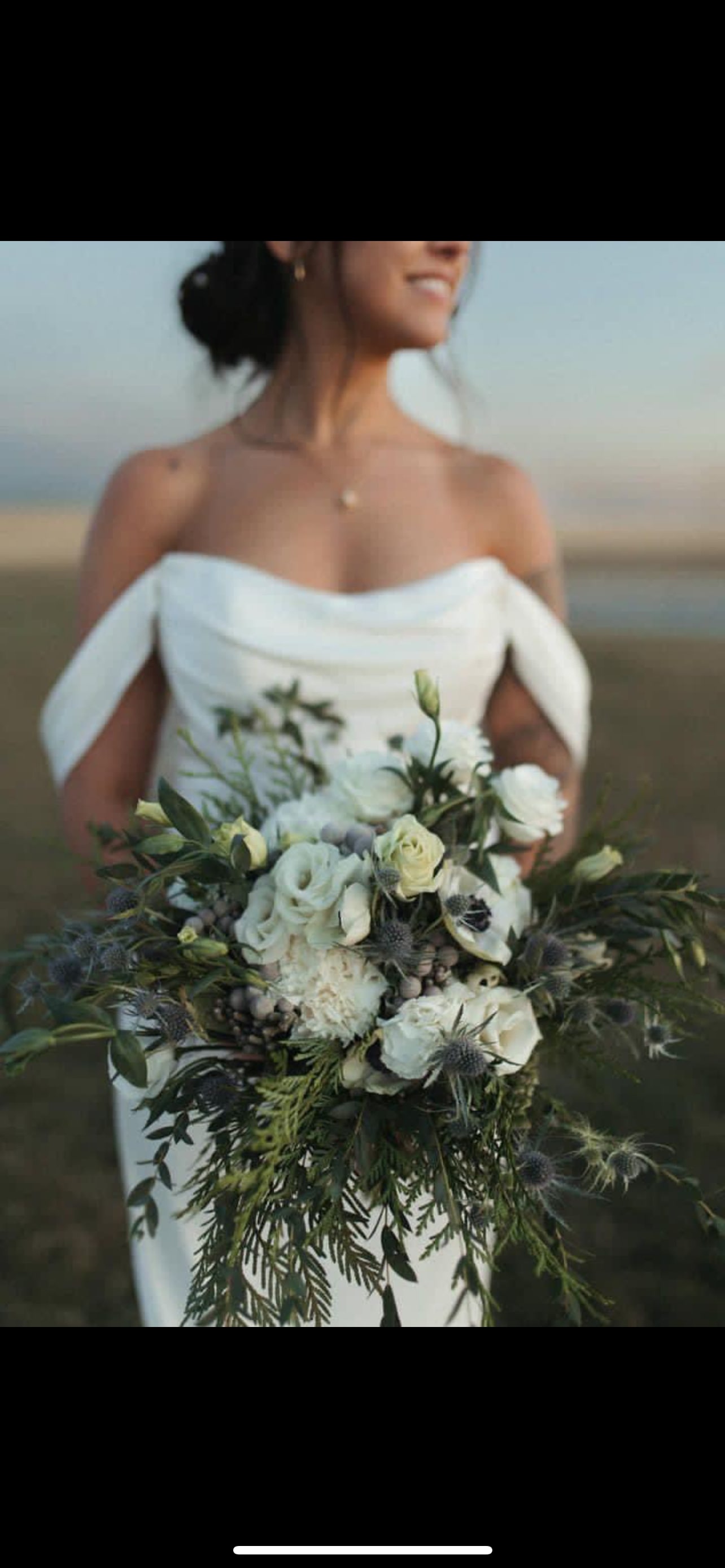 Bride holding a white and green bouquet with roses and thistle