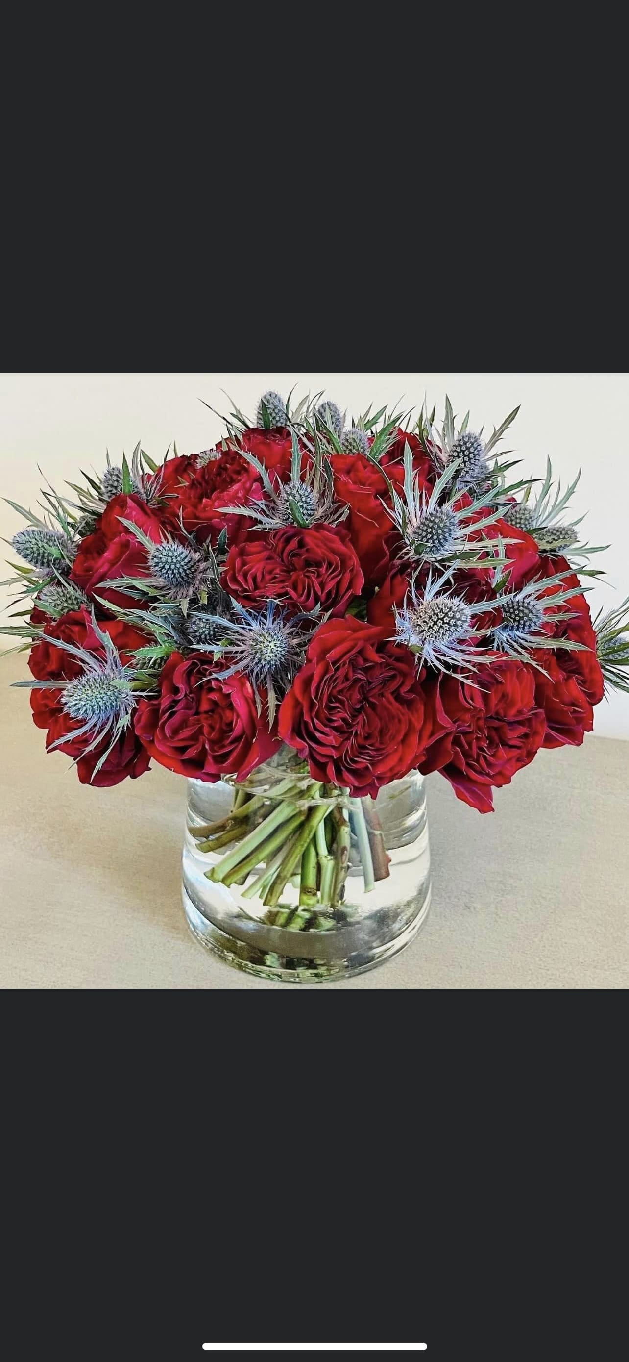 Red roses arranged in a clear glass vase with blue thistle accents.