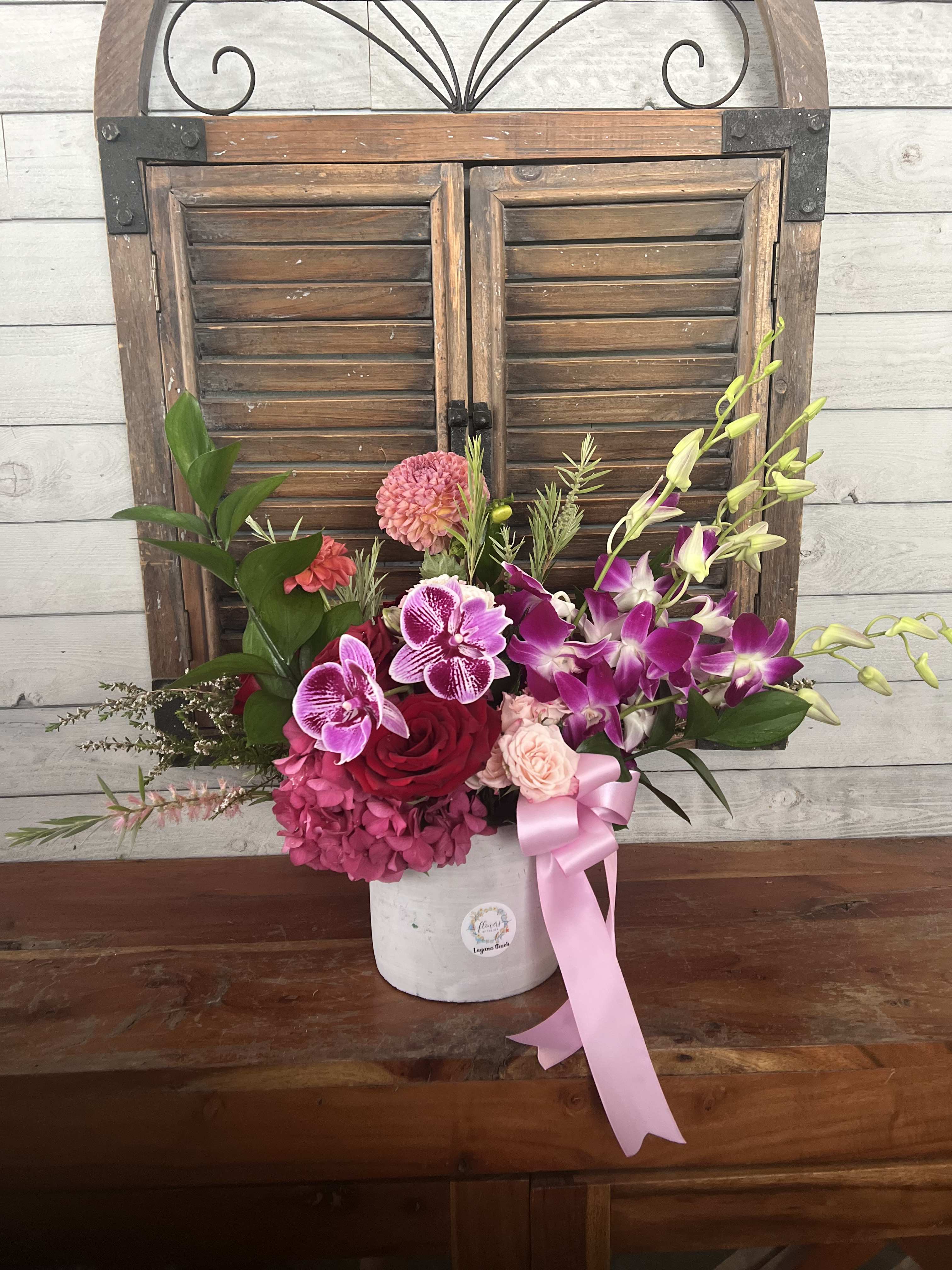 Pink and purple floral arrangement in a white vase with a pink ribbon