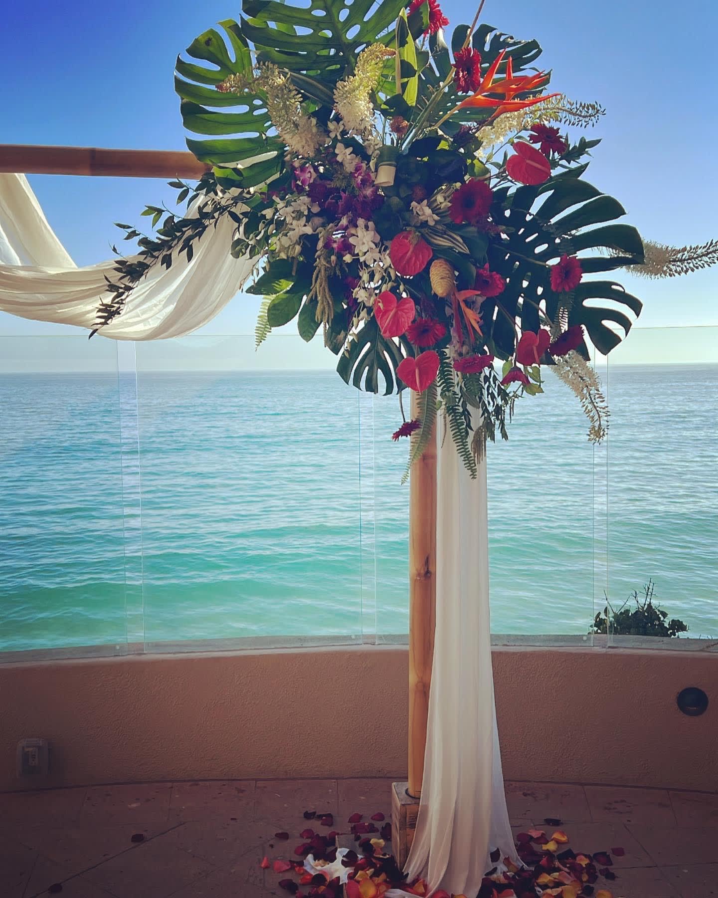 Tropical floral arch with red blooms and white draping by the ocean