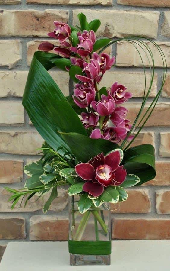Purple orchids arranged in a tall glass vase with broad green leaves