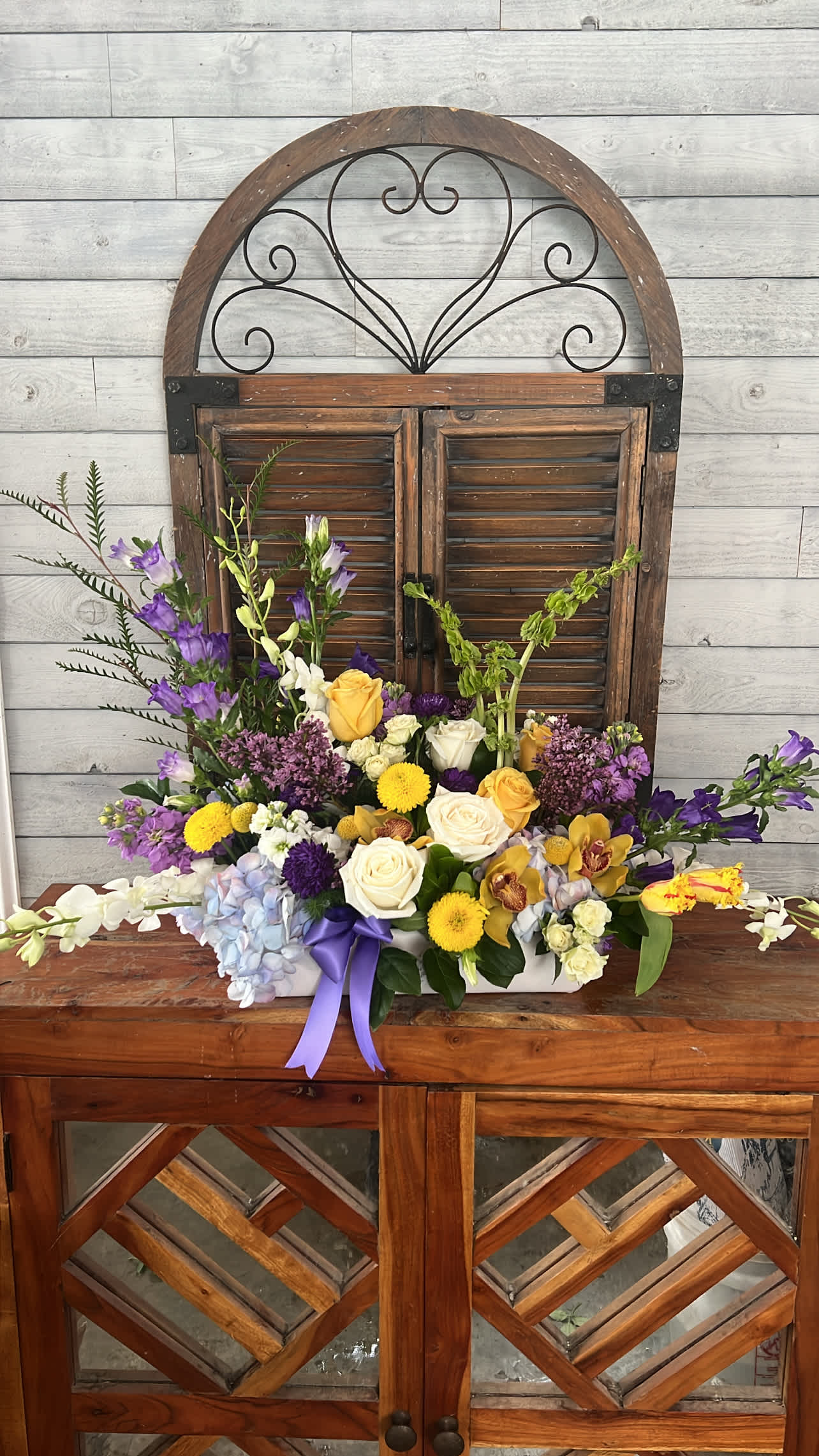 Mixed flower arrangement with roses, orchids, and purple blooms in a white container