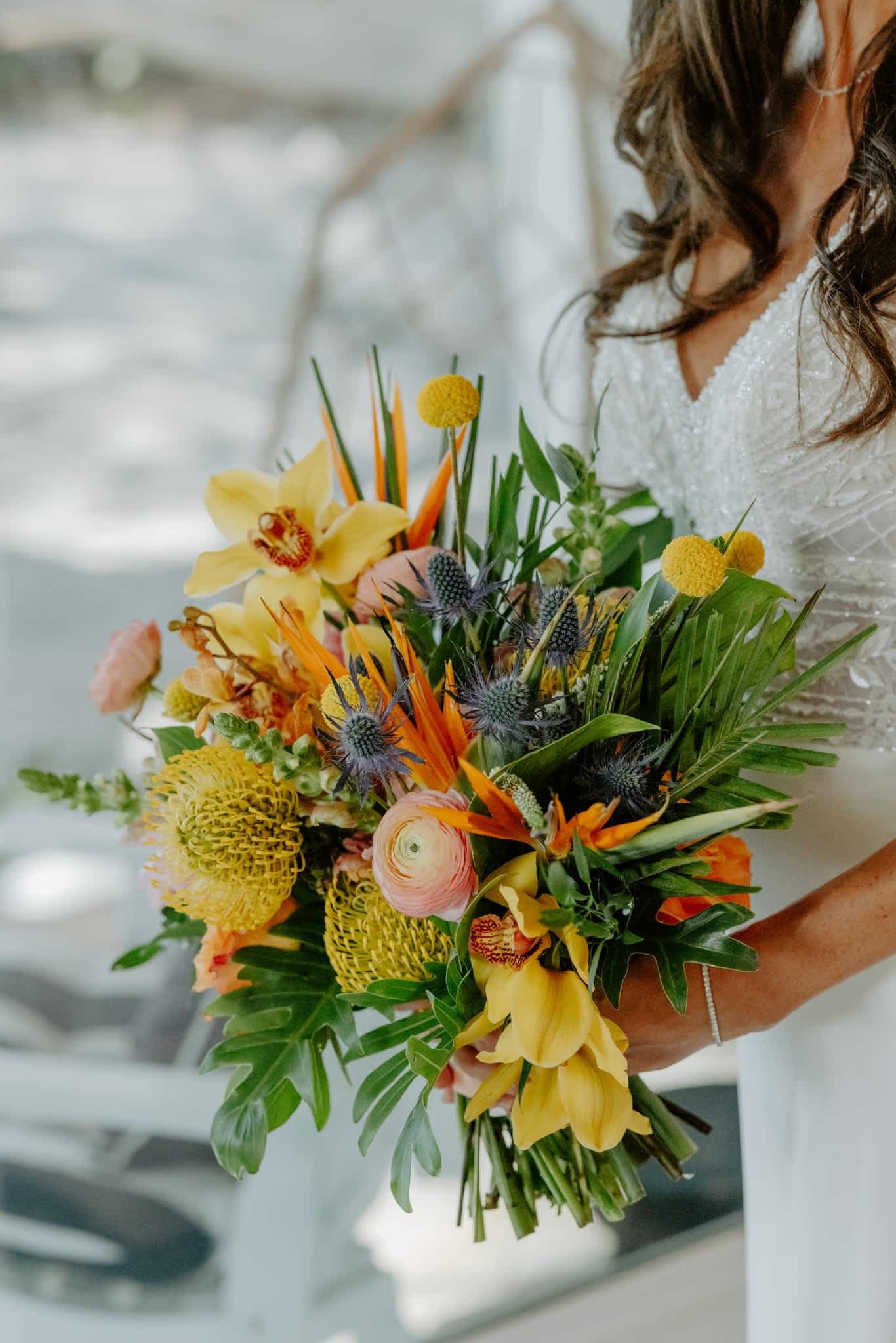 Bride holding a colorful tropical bouquet with yellow orchids and orange blooms