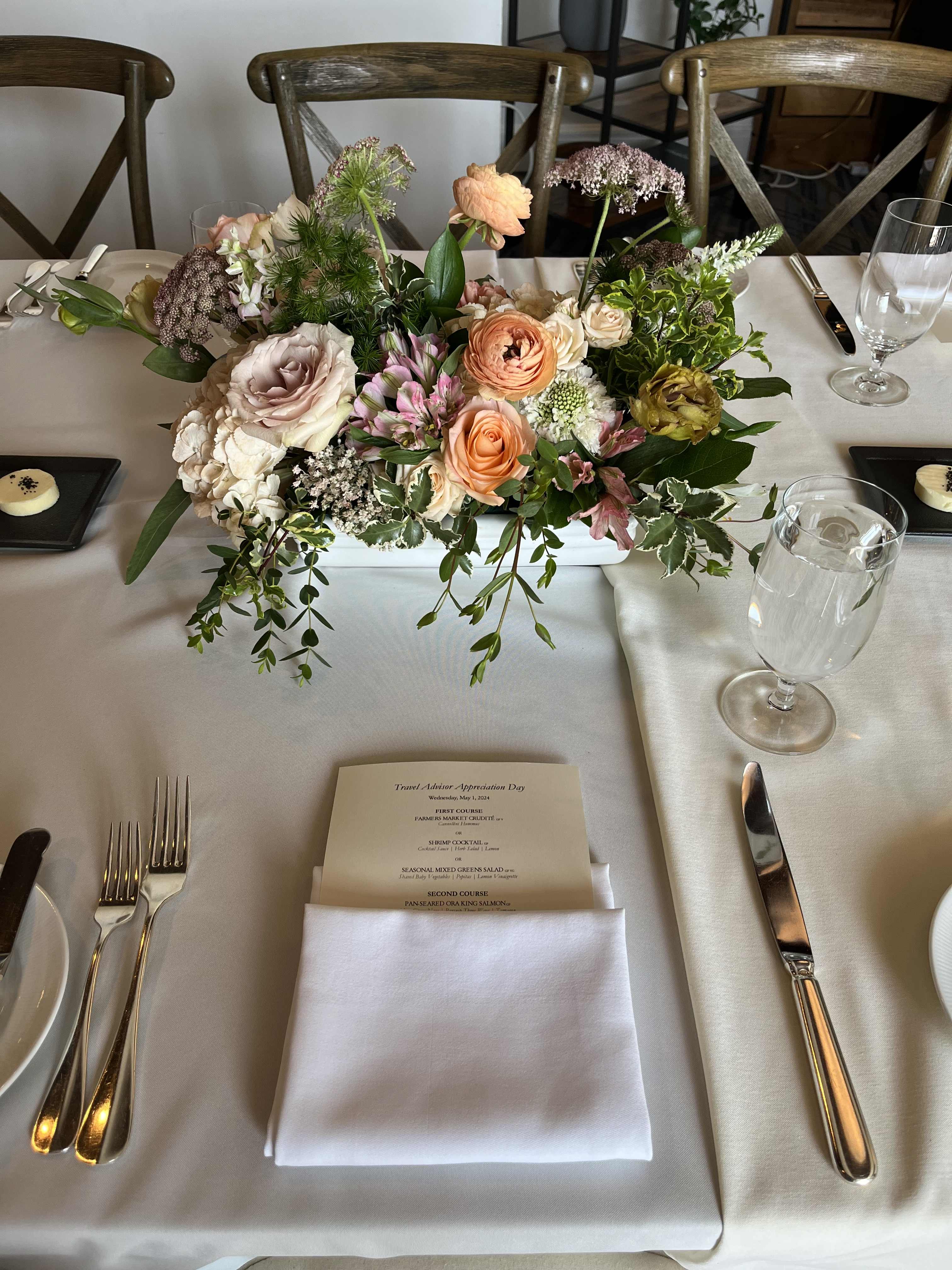 Low floral centerpiece with peach, blush, and white blooms on a dining table