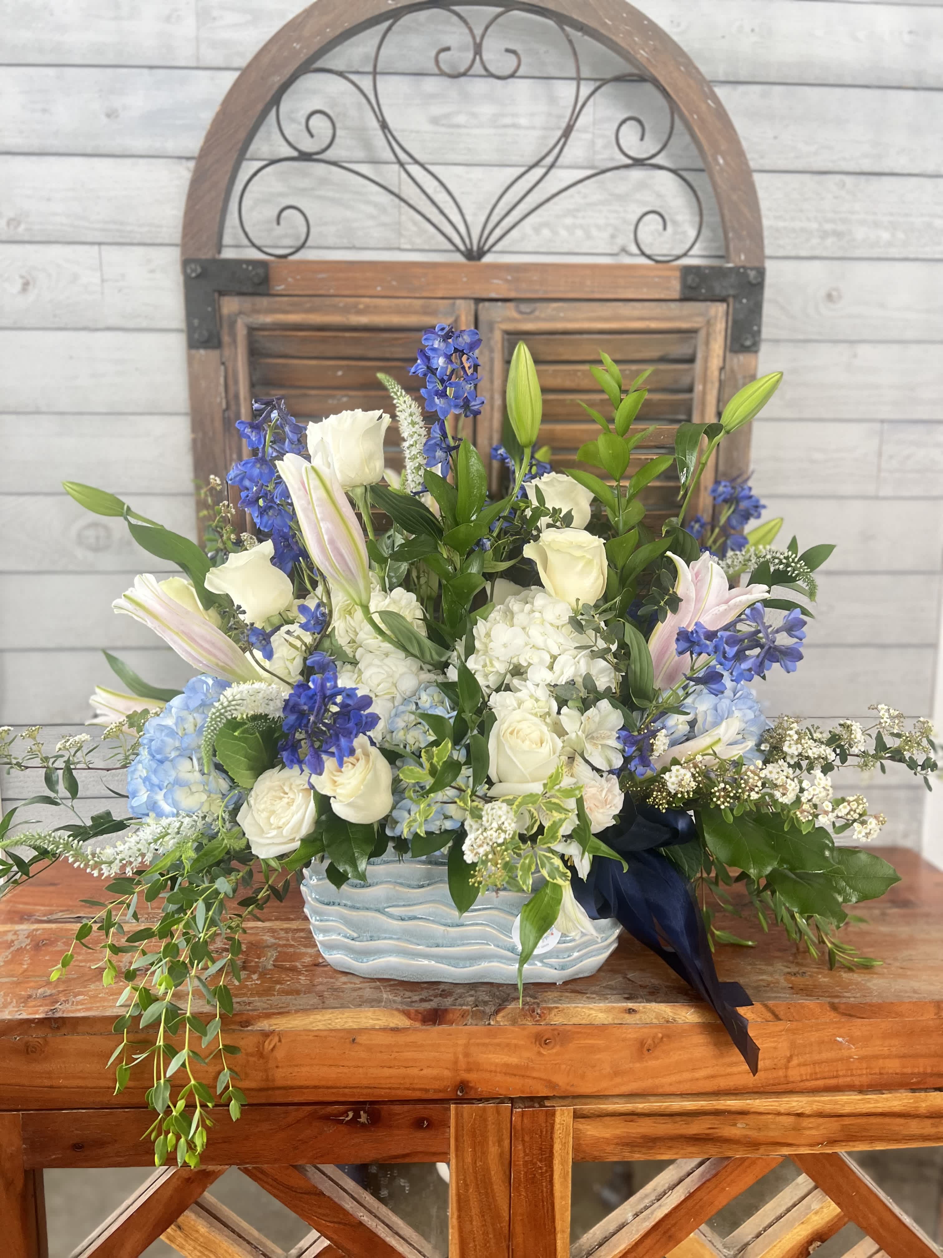 Blue and white floral arrangement in a ceramic vase with trailing greenery