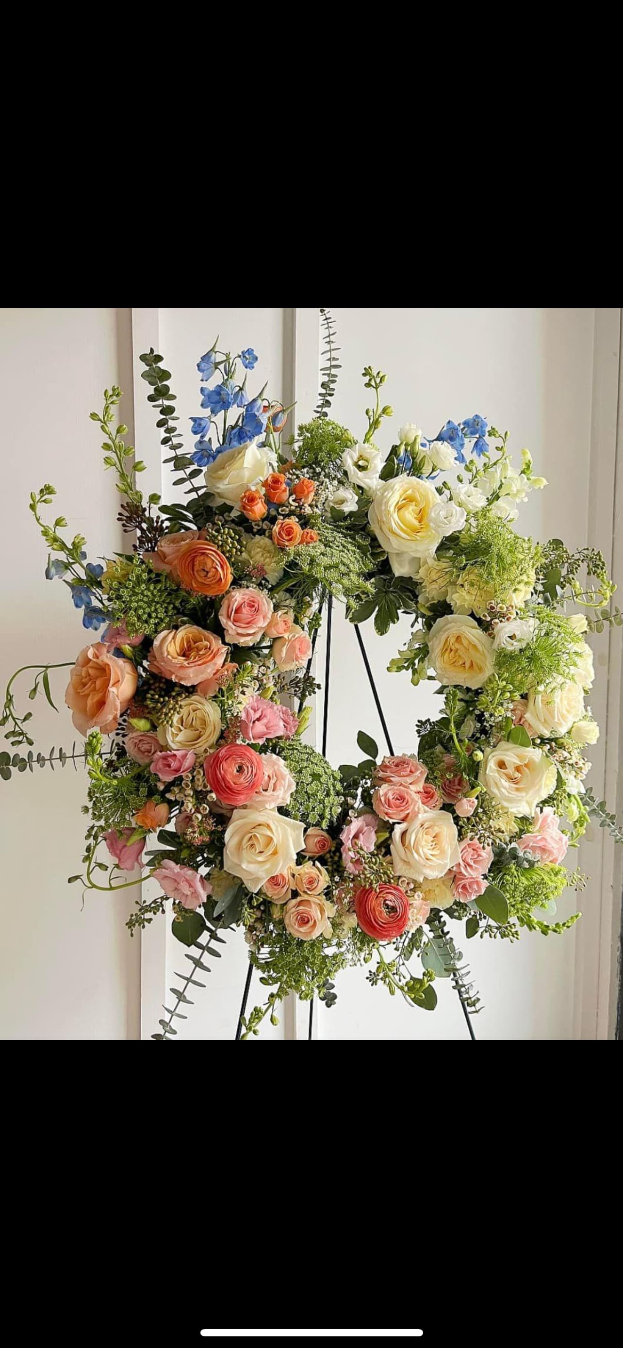 Large floral wreath with roses, ranunculus, and blue delphinium on a stand