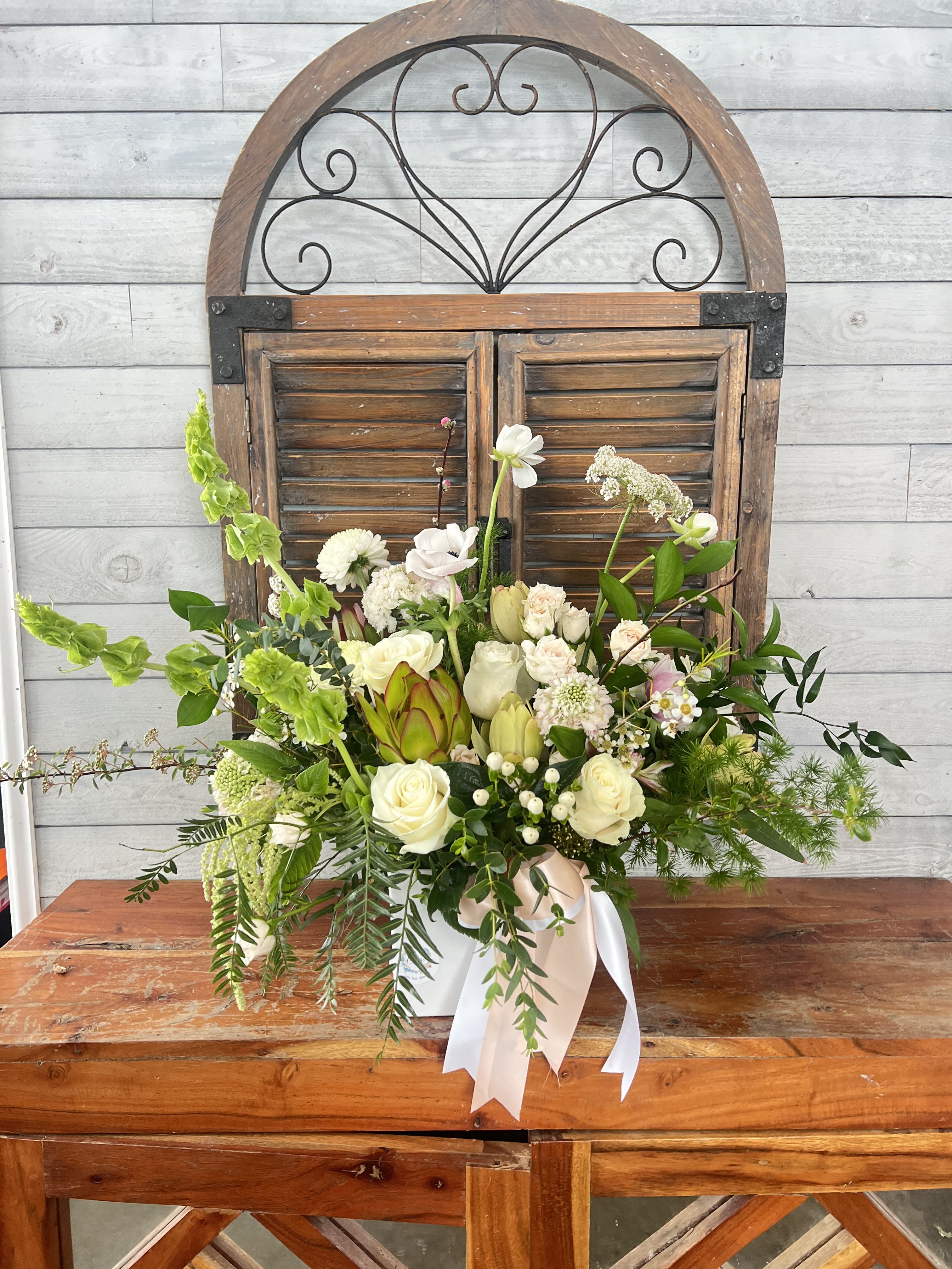 White and green floral arrangement in a white container with ribbon