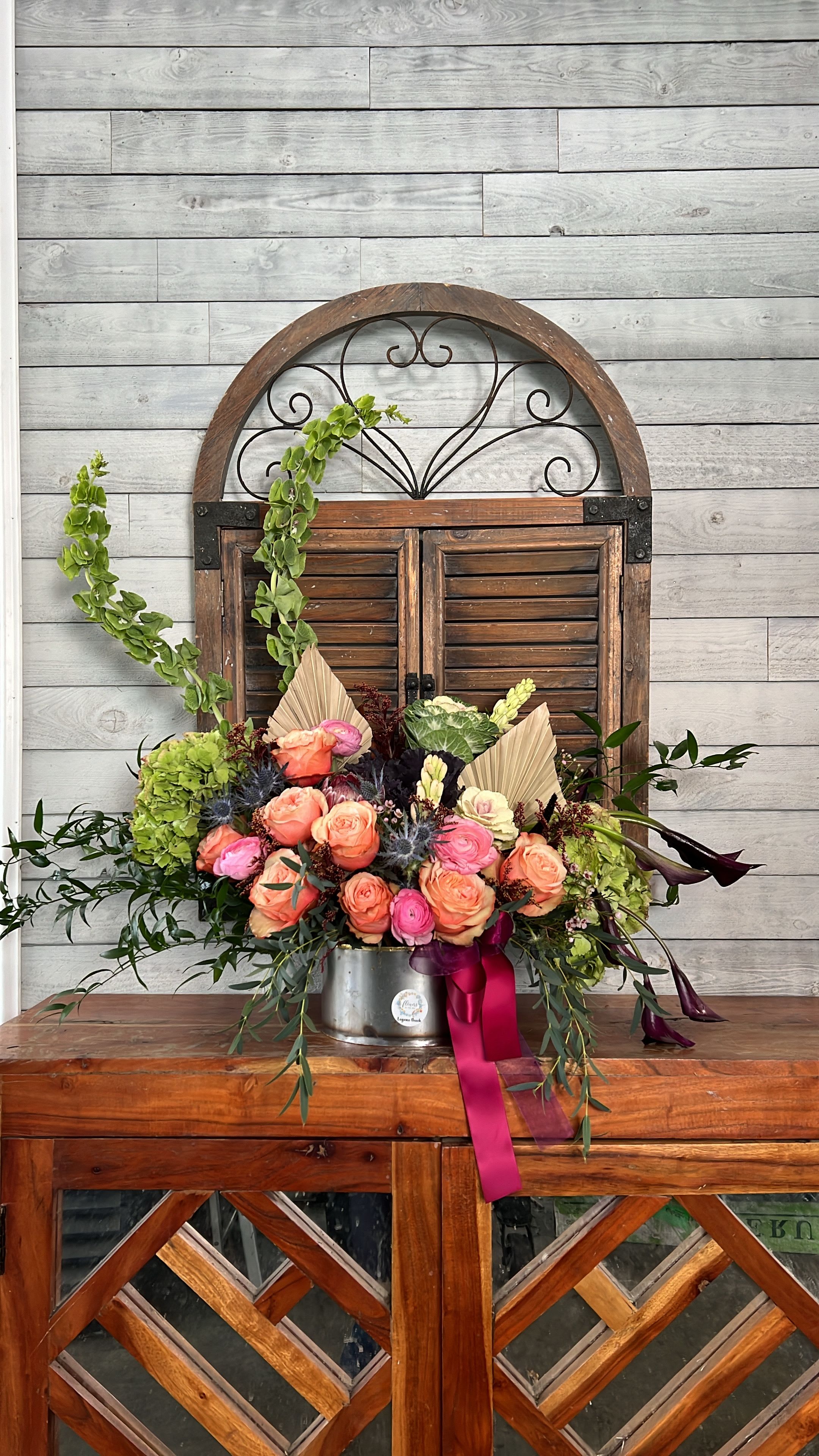 Peach and pink rose arrangement in a metal container with ribbon