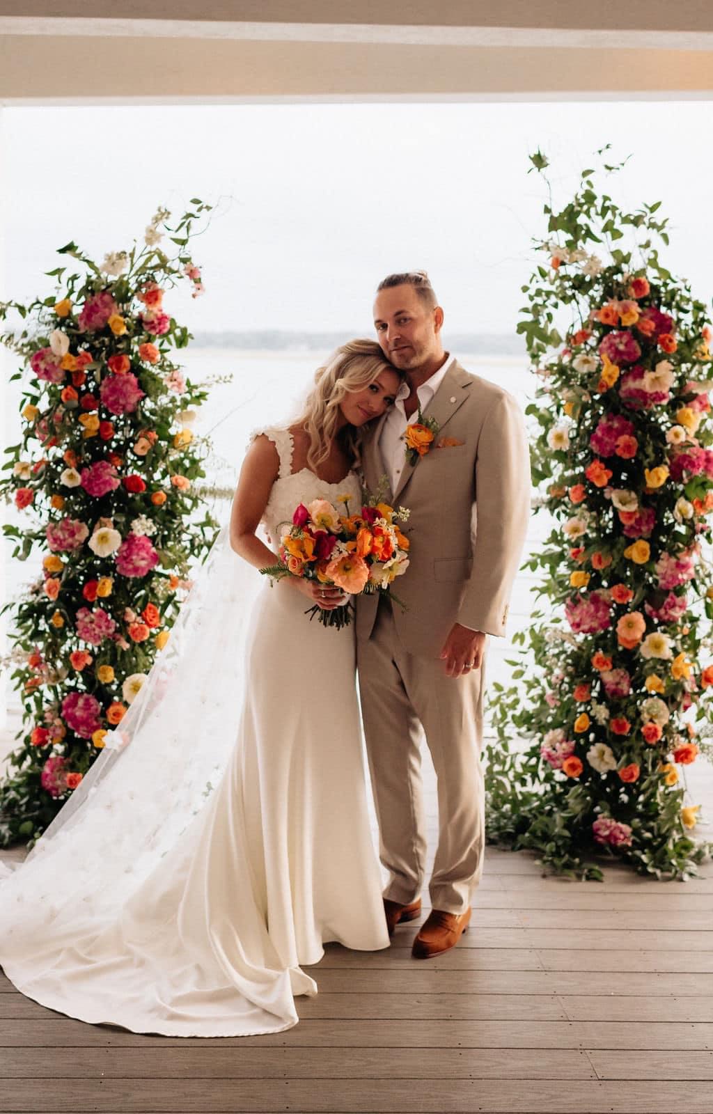 Bride and groom with colorful floral wedding arch and bouquet