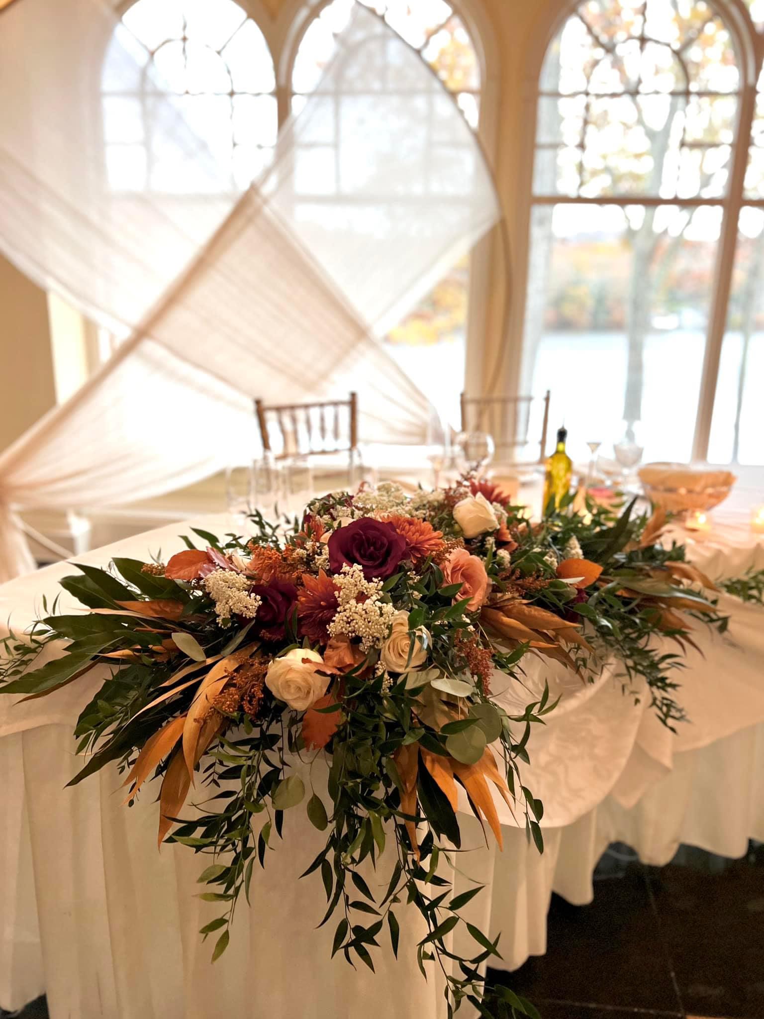 Low floral centerpiece with burgundy, peach, and cream blooms on a draped table