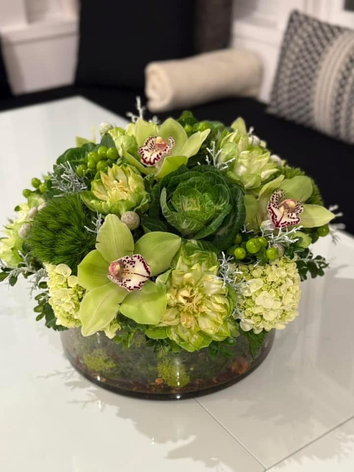 Green floral arrangement in a low glass bowl with orchids and hydrangeas