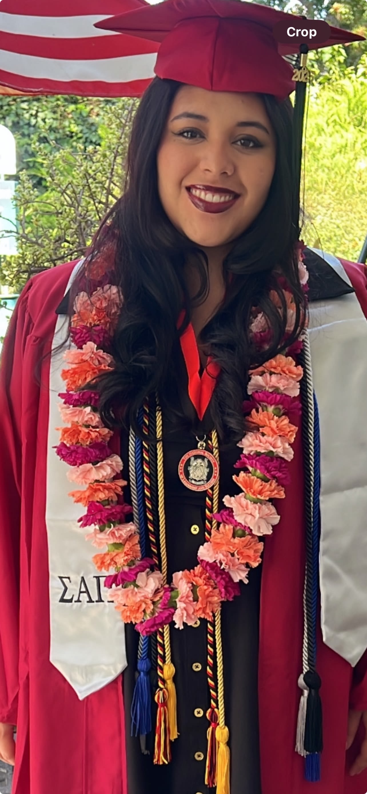 Graduate in maroon cap and gown with a flower lei