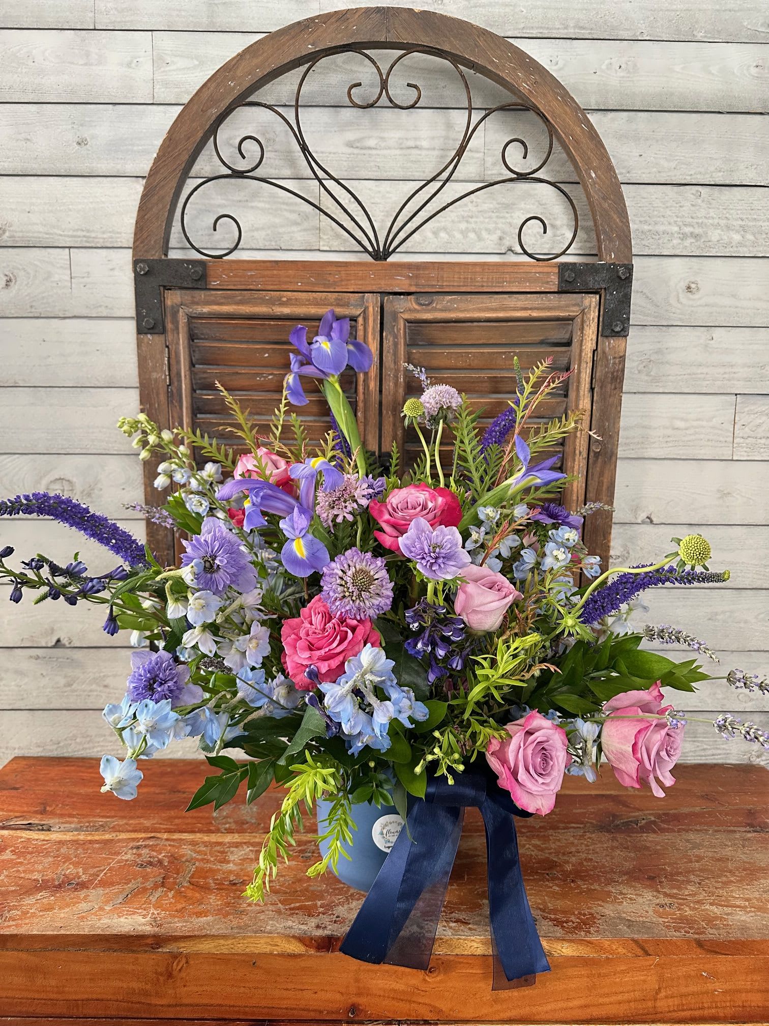 Mixed bouquet of pink and purple flowers in a blue vase with a ribbon