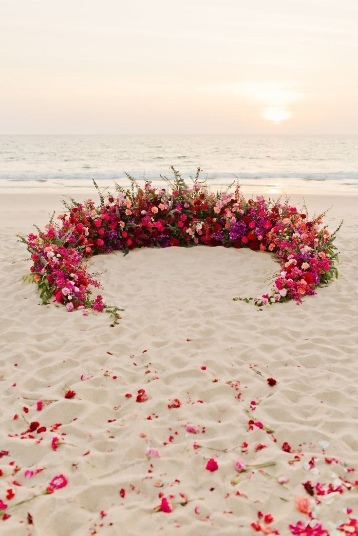 Large crescent-shaped floral arrangement on a beach at sunset