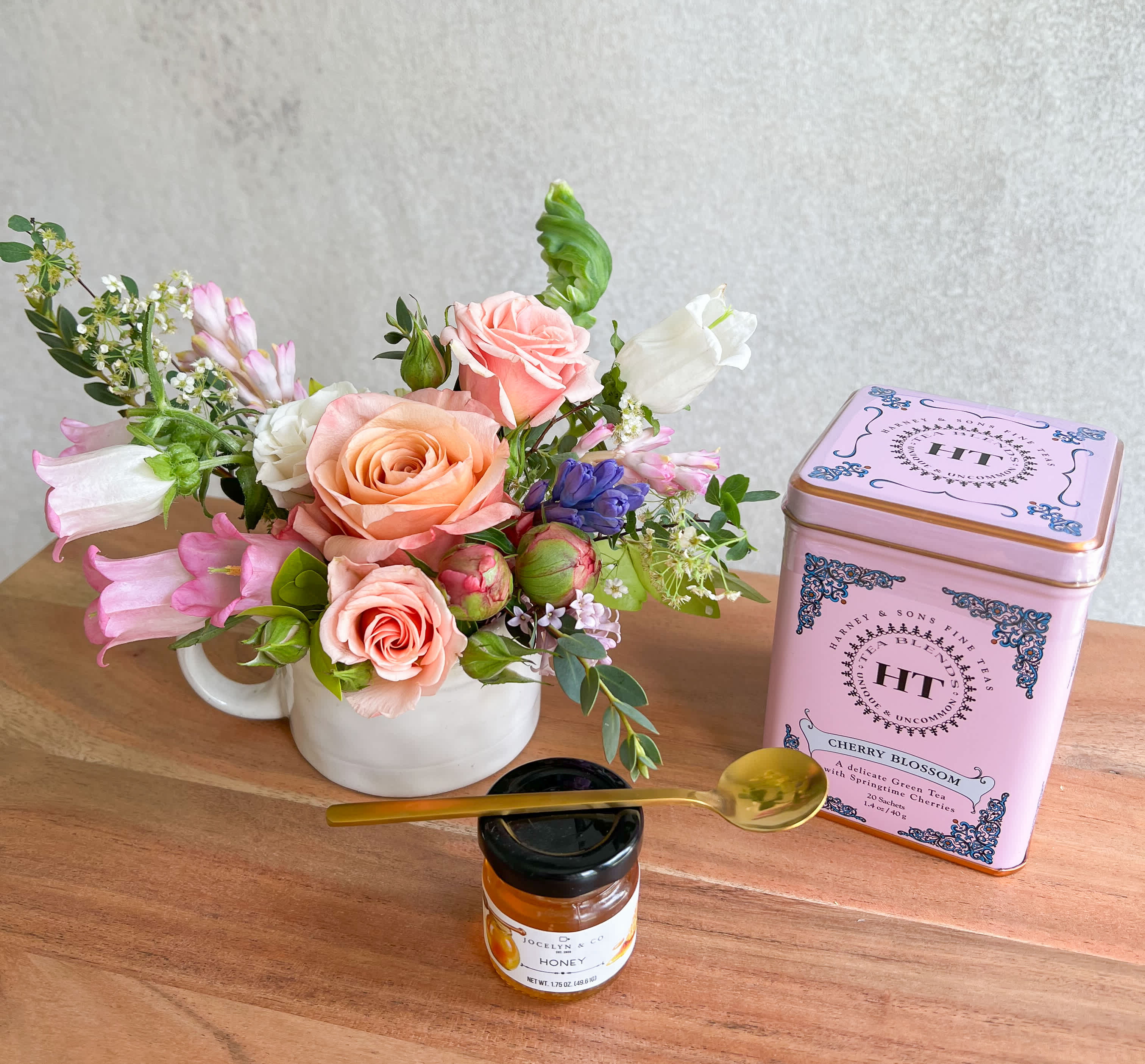 Pink and peach rose arrangement in a white mug with tea and honey gift items