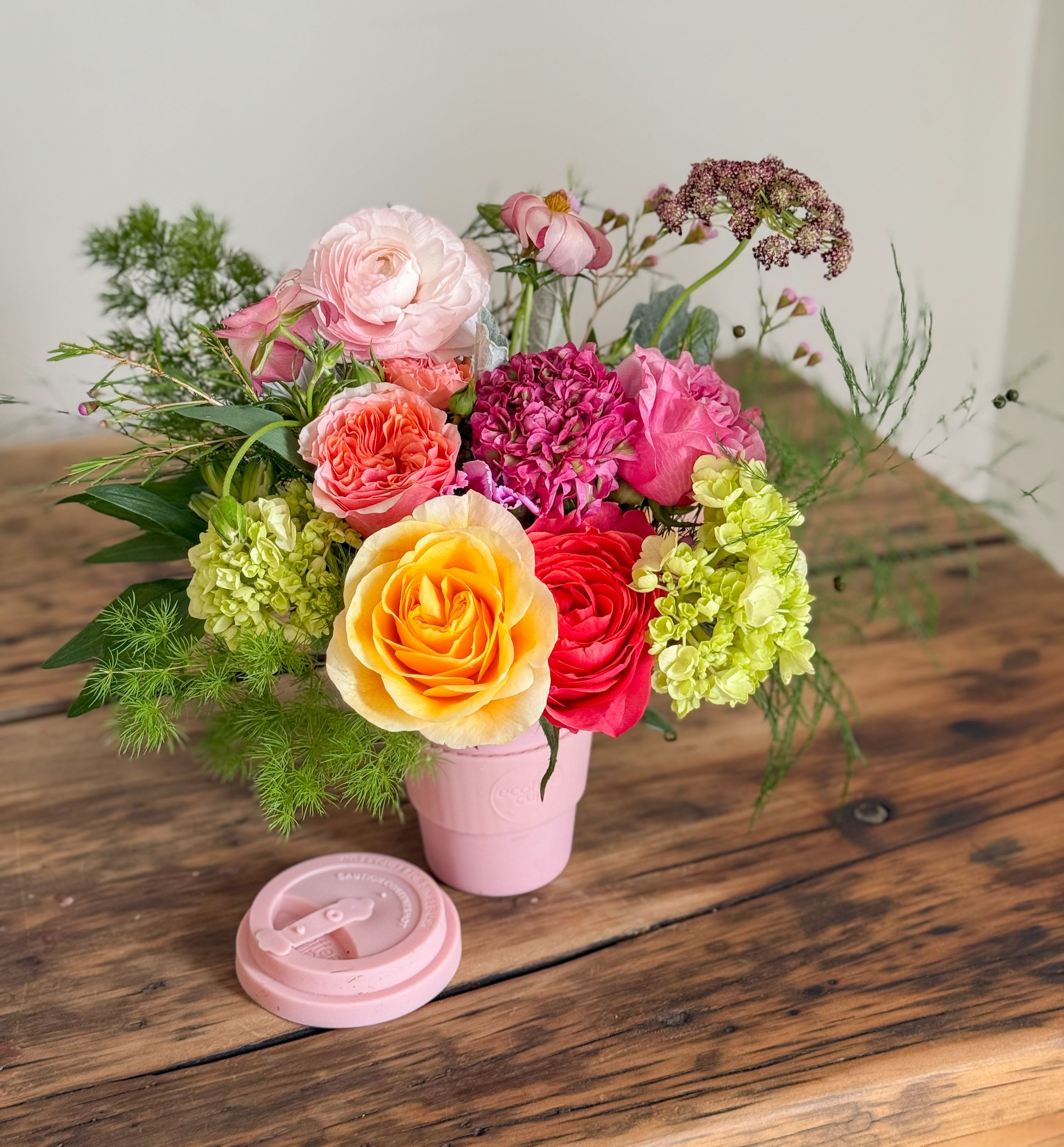 Mixed bouquet of roses and hydrangeas in a pink cup-style vase