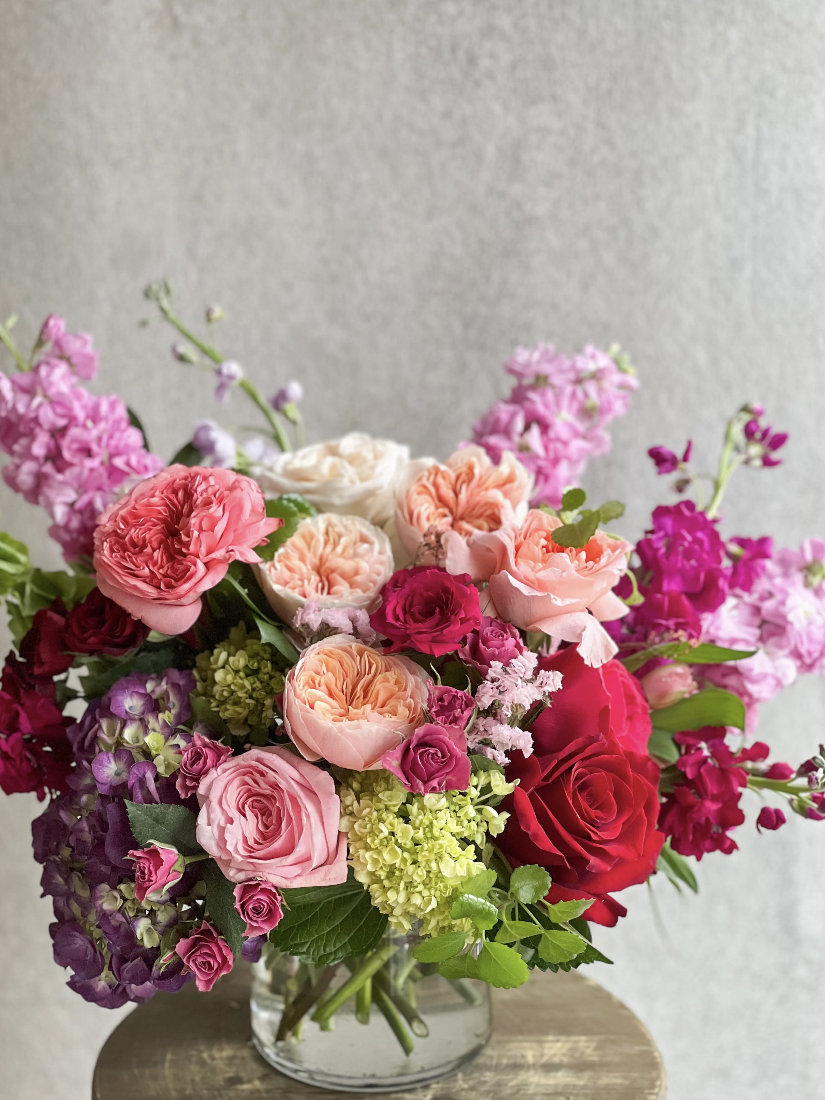Pink and red roses arranged in a clear glass vase with purple blooms