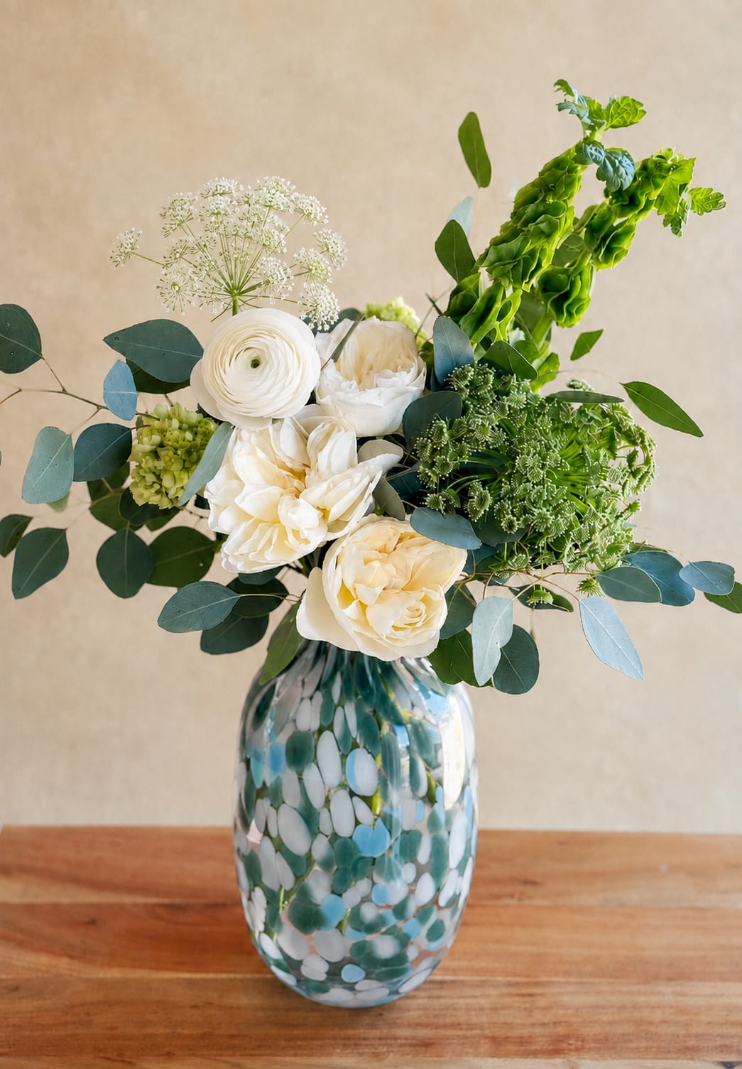 White flowers in a patterned glass vase with blue-green foliage