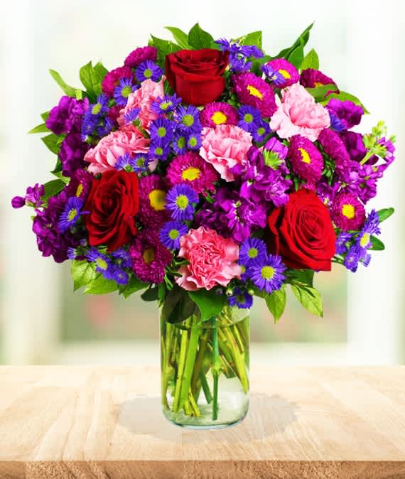 Bouquet of red roses, pink carnations, and purple daisies in a glass vase