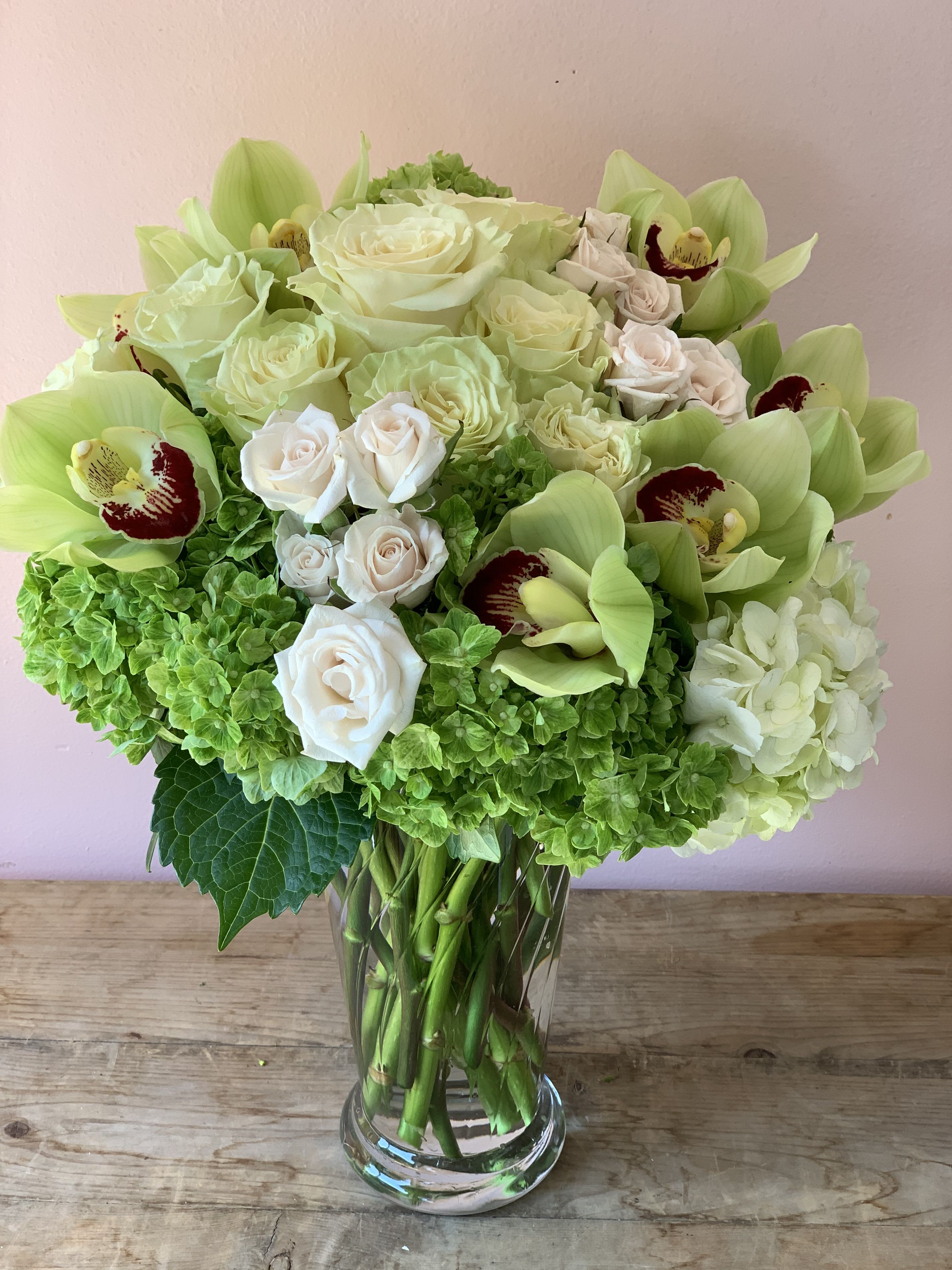 Bouquet of pale roses, green orchids, and hydrangeas in a glass vase