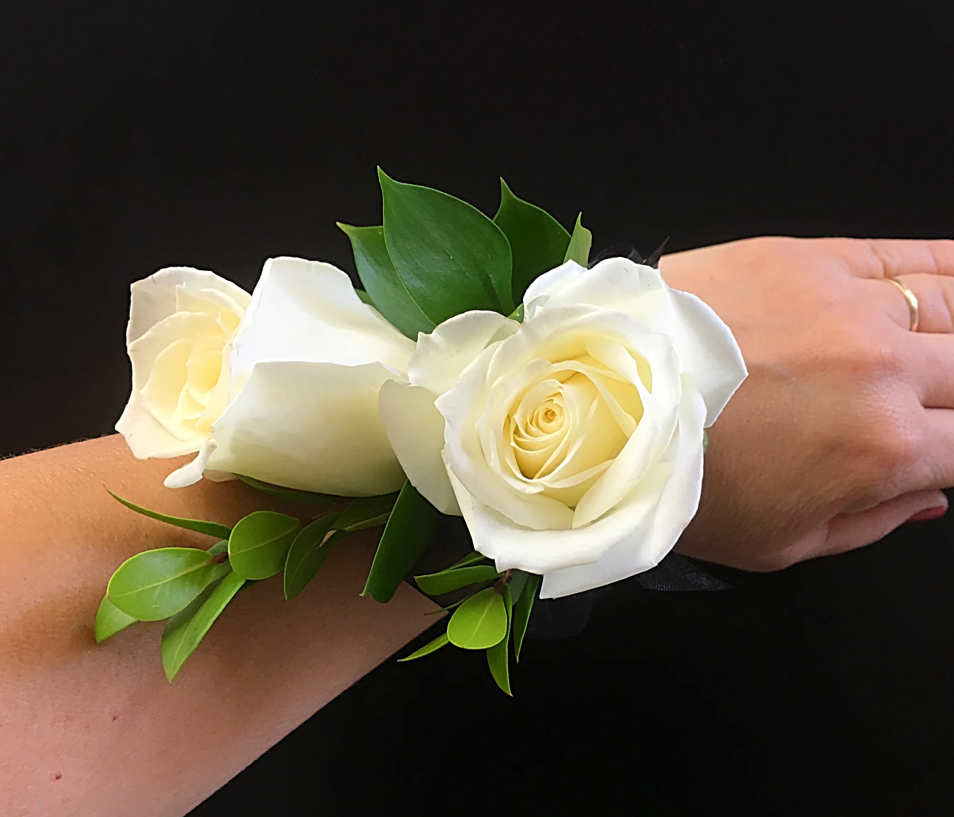 White rose wrist corsage with green leaves on a black ribbon