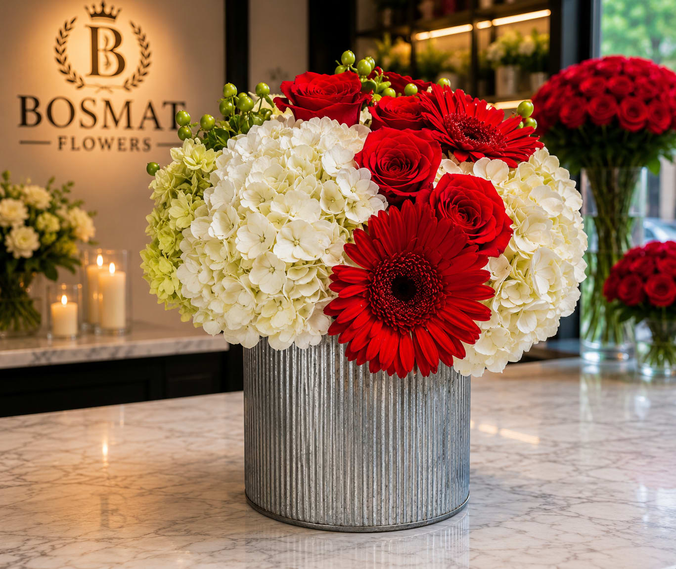 Red roses and gerbera daisies arranged with white hydrangeas in a ribbed metal vase.