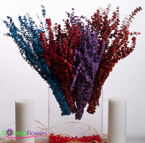Tall multicolored floral arrangement in a clear vase with two white candles