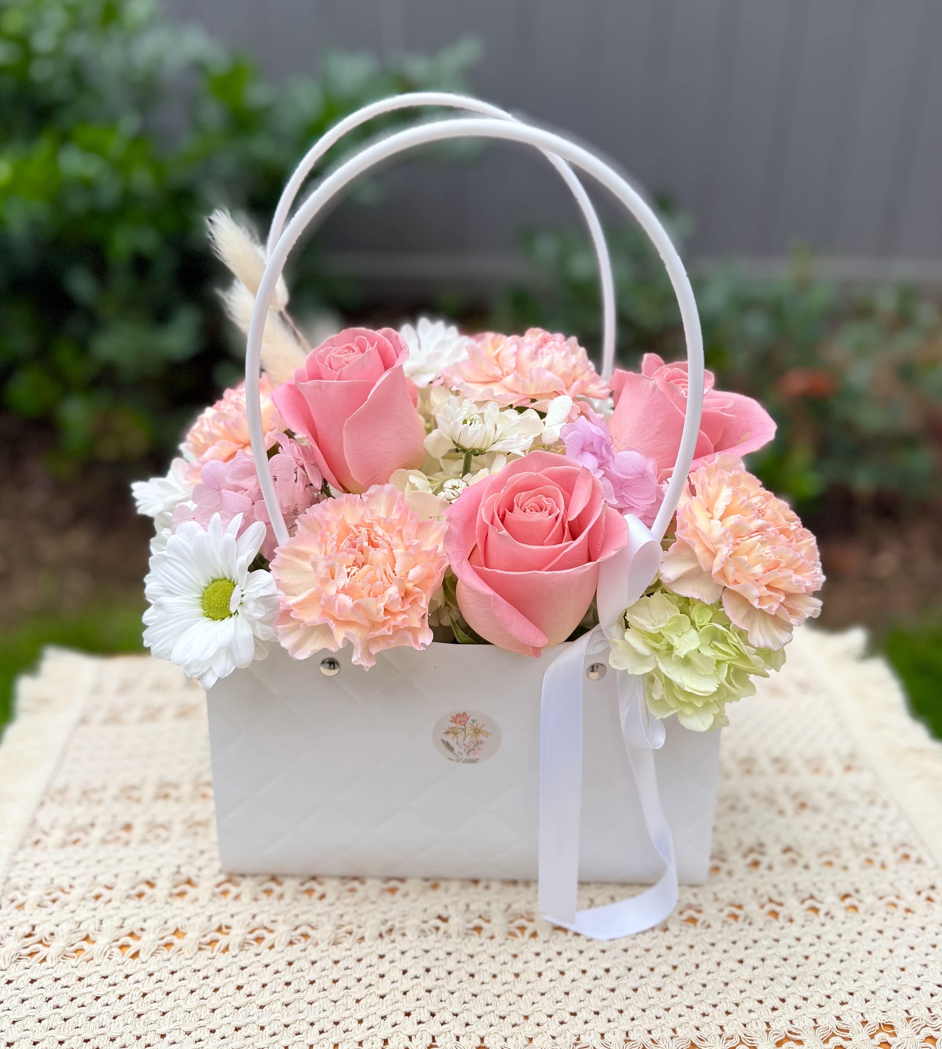 Pink roses and pastel flowers arranged in a white basket with ribbon