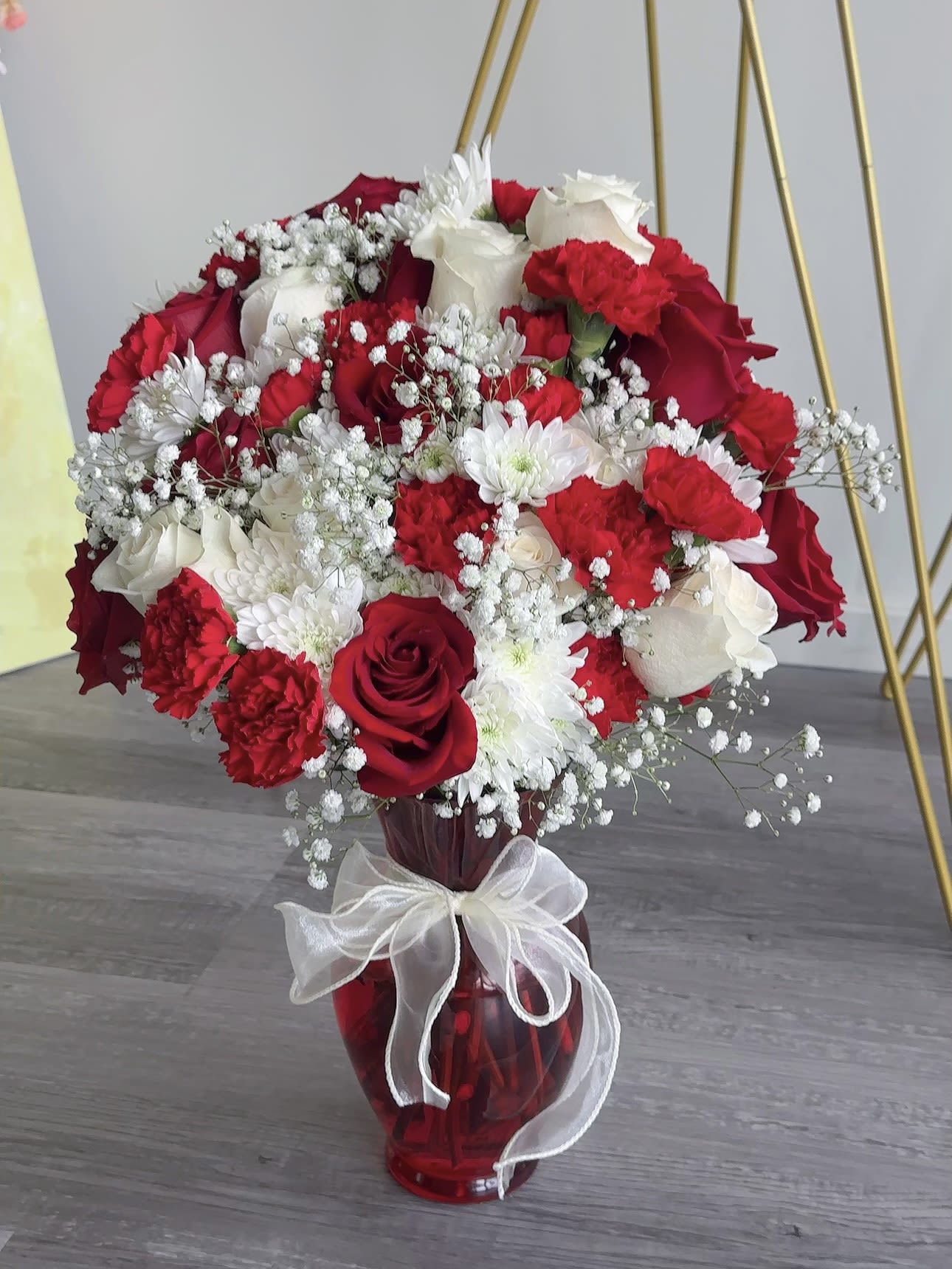 Red and white rose bouquet in a red glass vase with a white ribbon