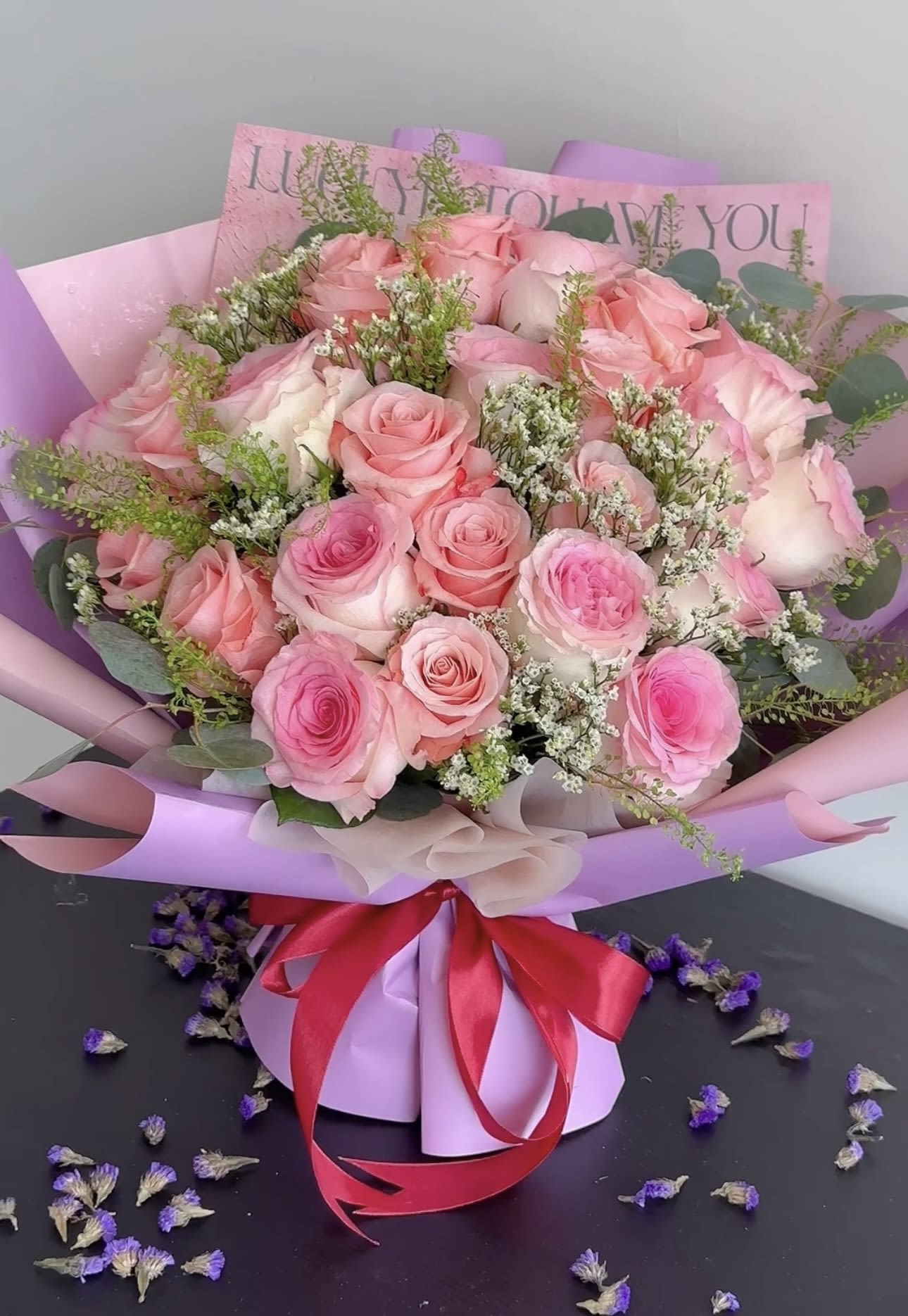 Pink rose bouquet wrapped in lavender paper with a red ribbon
