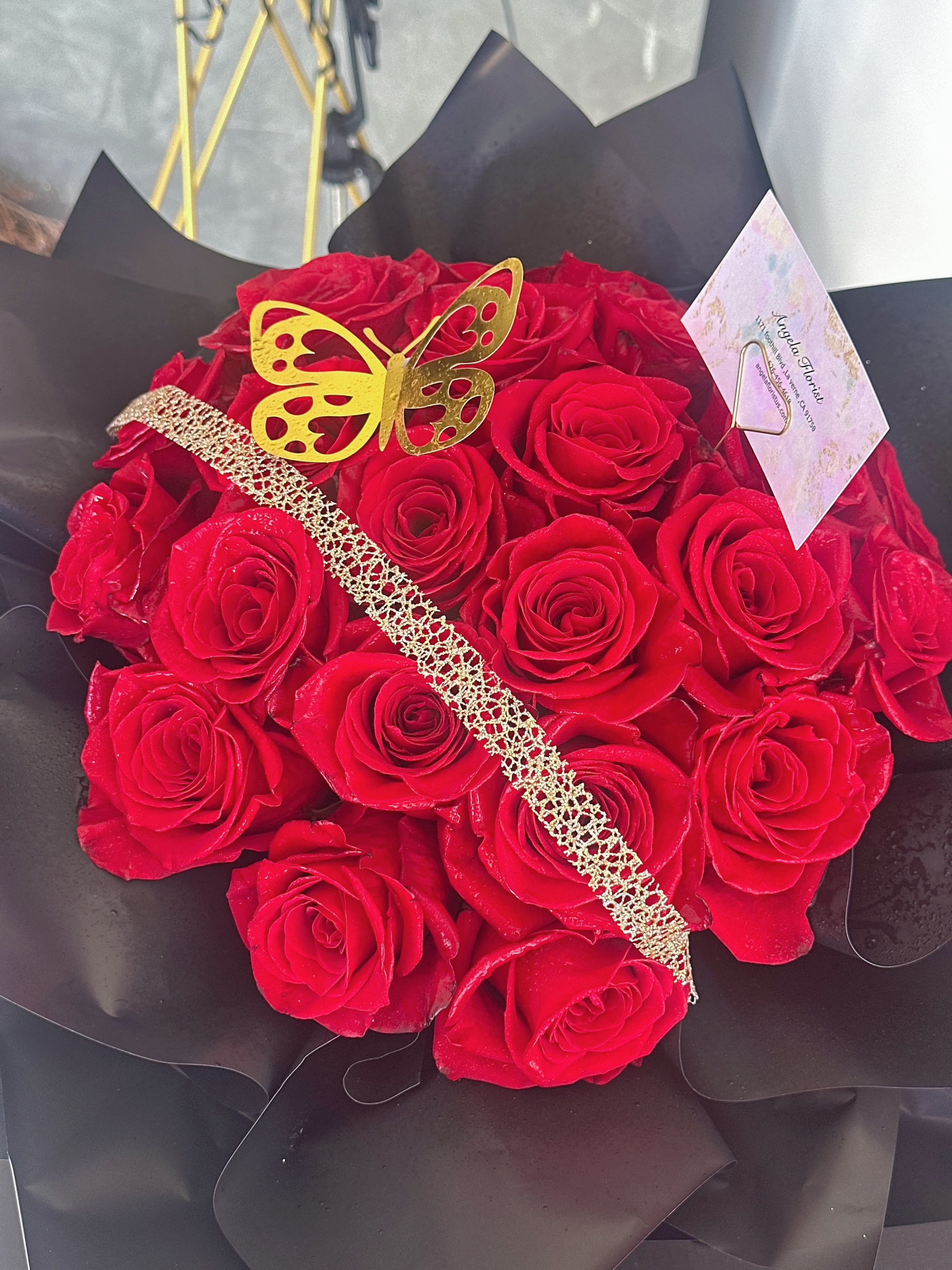 Bouquet of red roses wrapped in black paper with a gold butterfly decoration