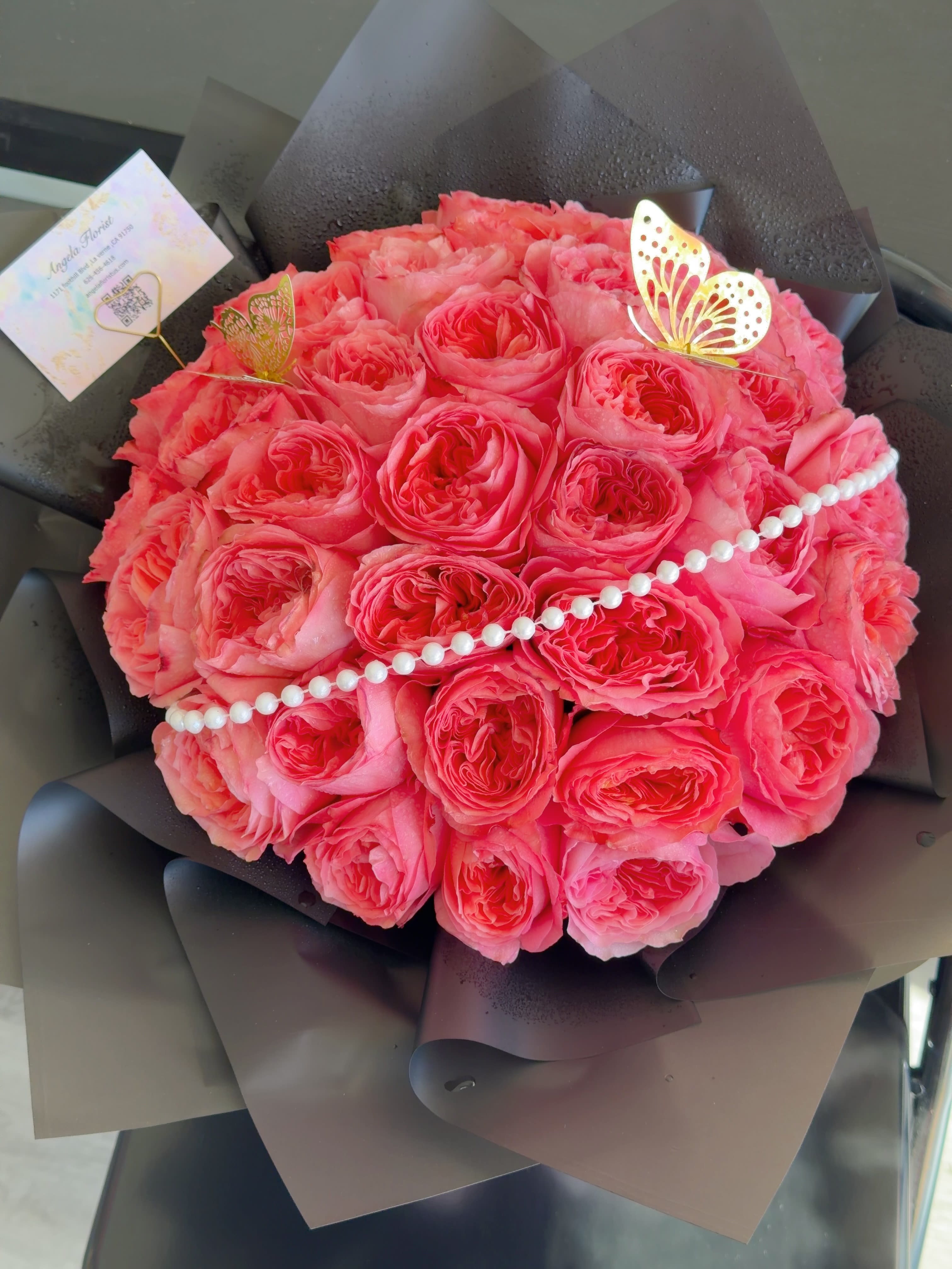 Round bouquet of pink roses wrapped in dark paper with pearl trim