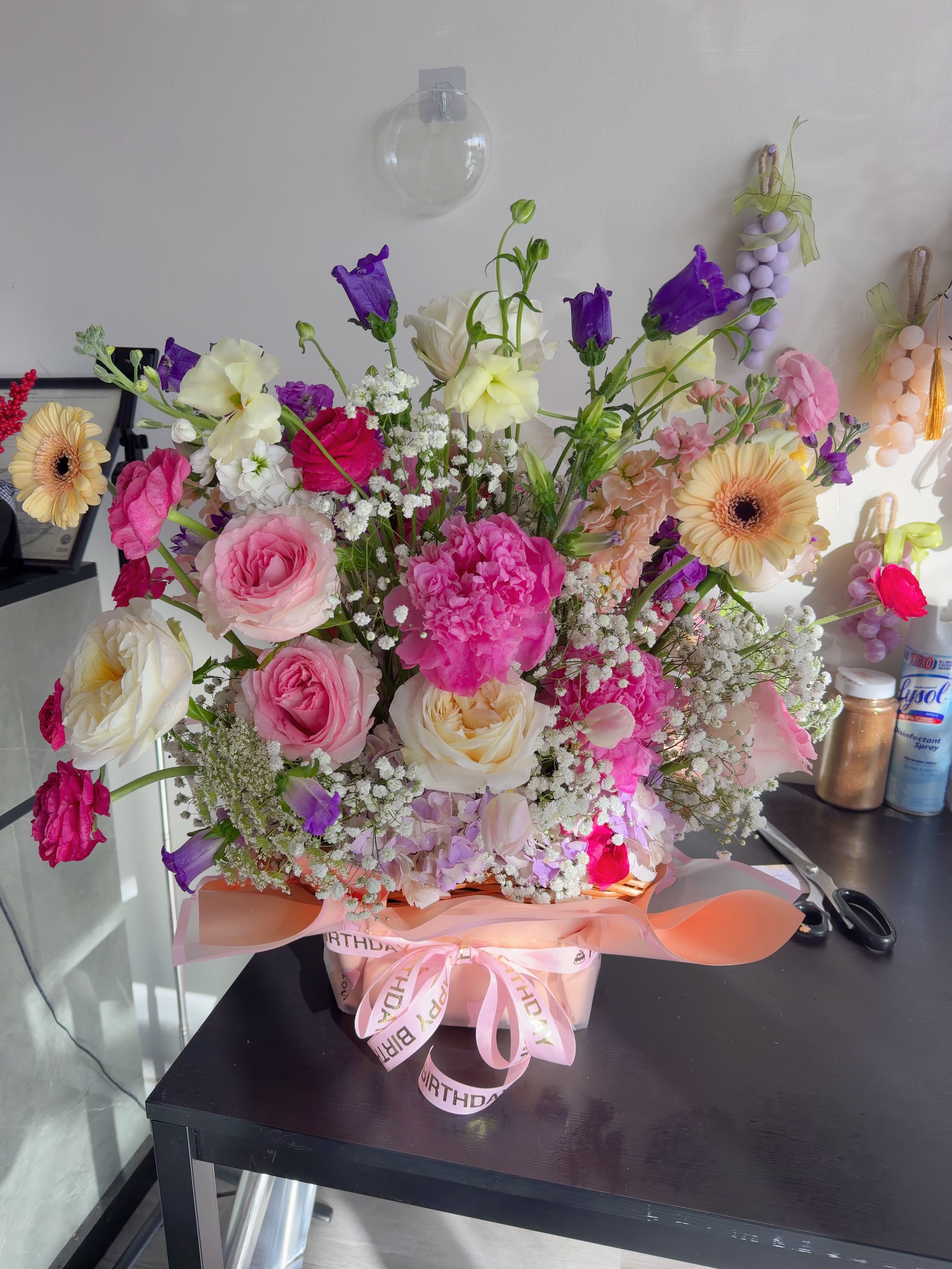 Blush Dream Bouquet - This elegant double-sided floral basket arrangement is designed to be admired from every angle. The flowers are arranged in floral foam and placed in a decorative basket, ensuring stability, hydration, and long-lasting freshness.  Featuring a romantic blend of premium seasonal blooms in soft pink, cream, lavender, and pastel tones, the arrangement creates a lush and airy garden-style look. The double-sided design makes it perfect for table displays, birthdays, celebrations, or thoughtful gifts.  Each piece is handcrafted to ensure balance, fullness, and beauty from both sides. A charming floral gift that brings color and elegance to any space. 