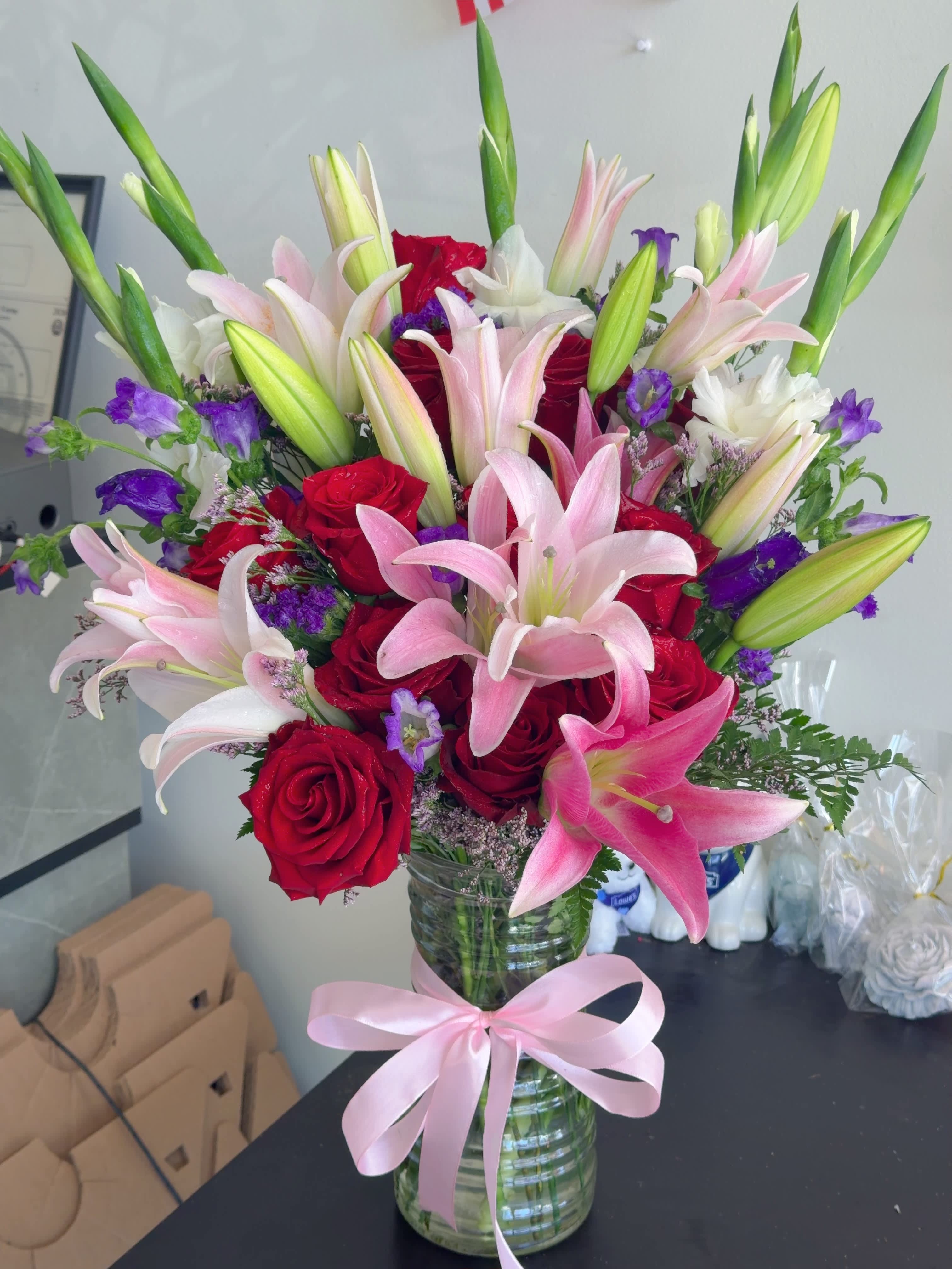 Bouquet of pink lilies and red roses in a glass vase with a pink ribbon