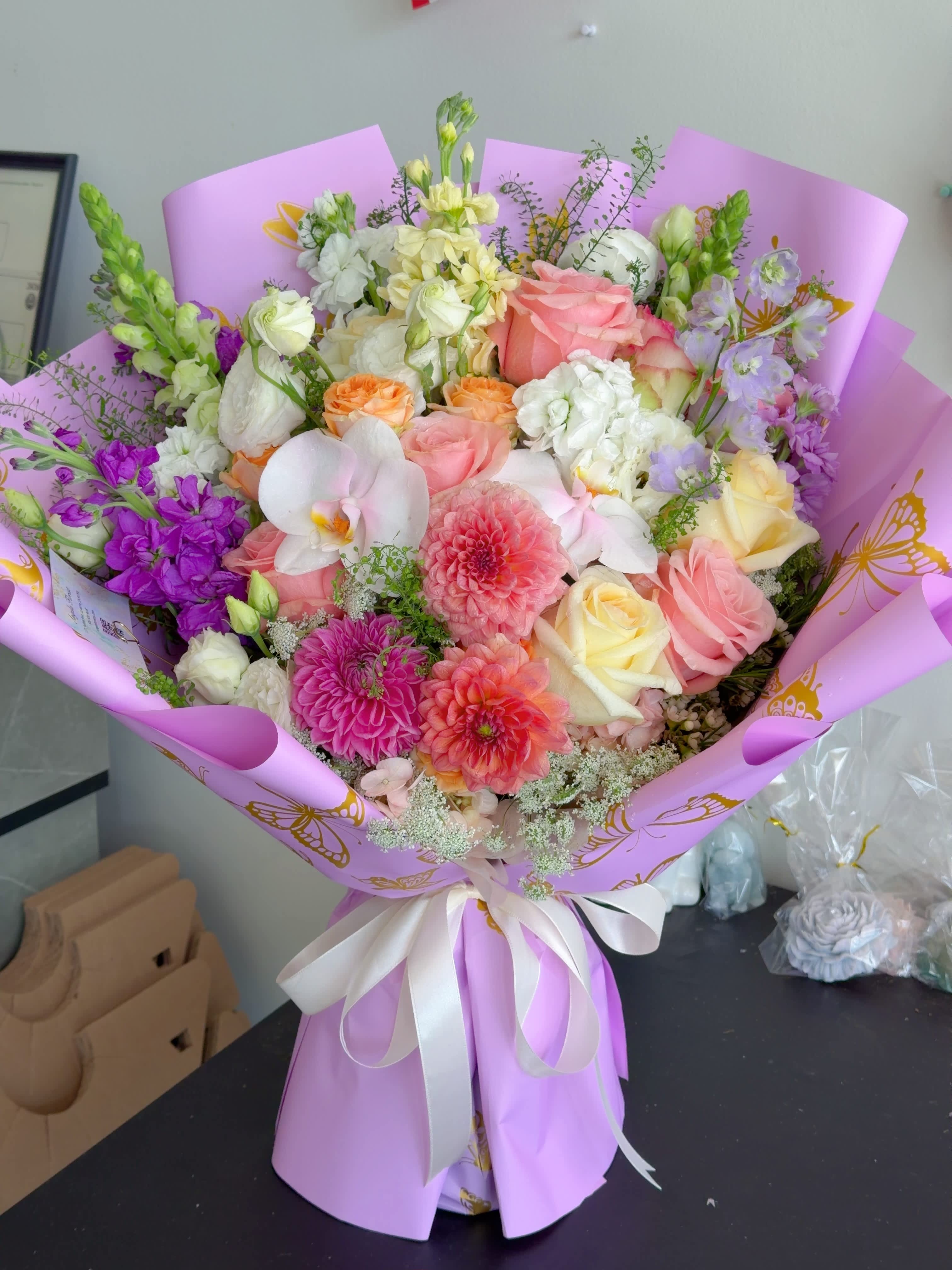 Mixed bouquet of pink, white, and purple flowers wrapped in lavender paper