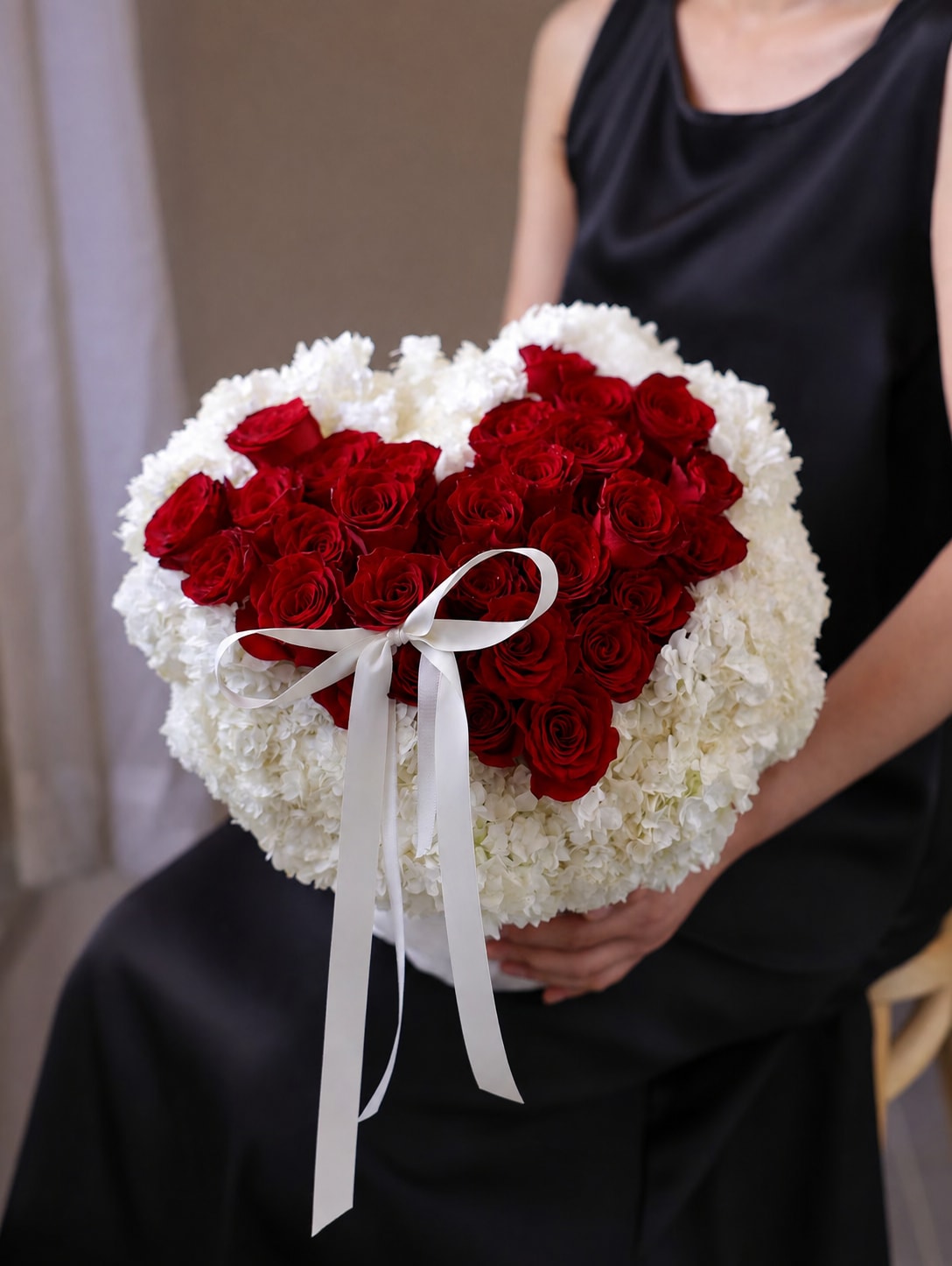 Heart-shaped bouquet of red roses and white flowers with a white ribbon