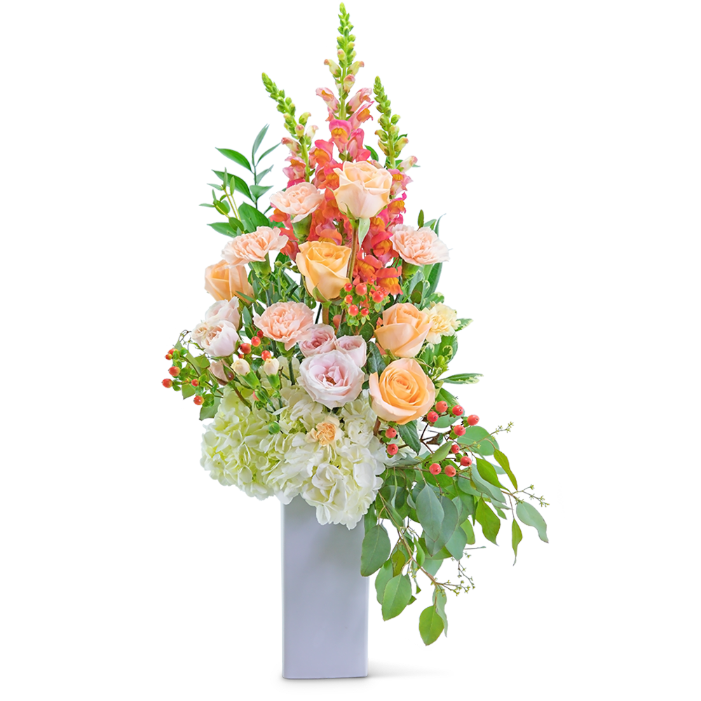 Tall floral arrangement with peach roses, pink snapdragons, and white hydrangeas in a white vase