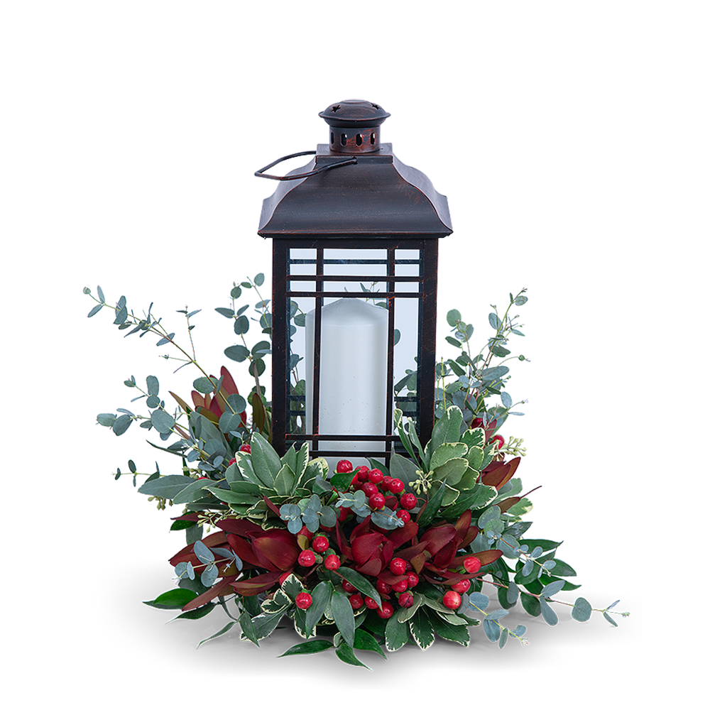 Black lantern with a white candle surrounded by red berries and greenery