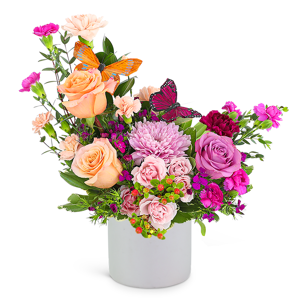 Mixed pink and peach flower arrangement in a white vase with butterfly picks
