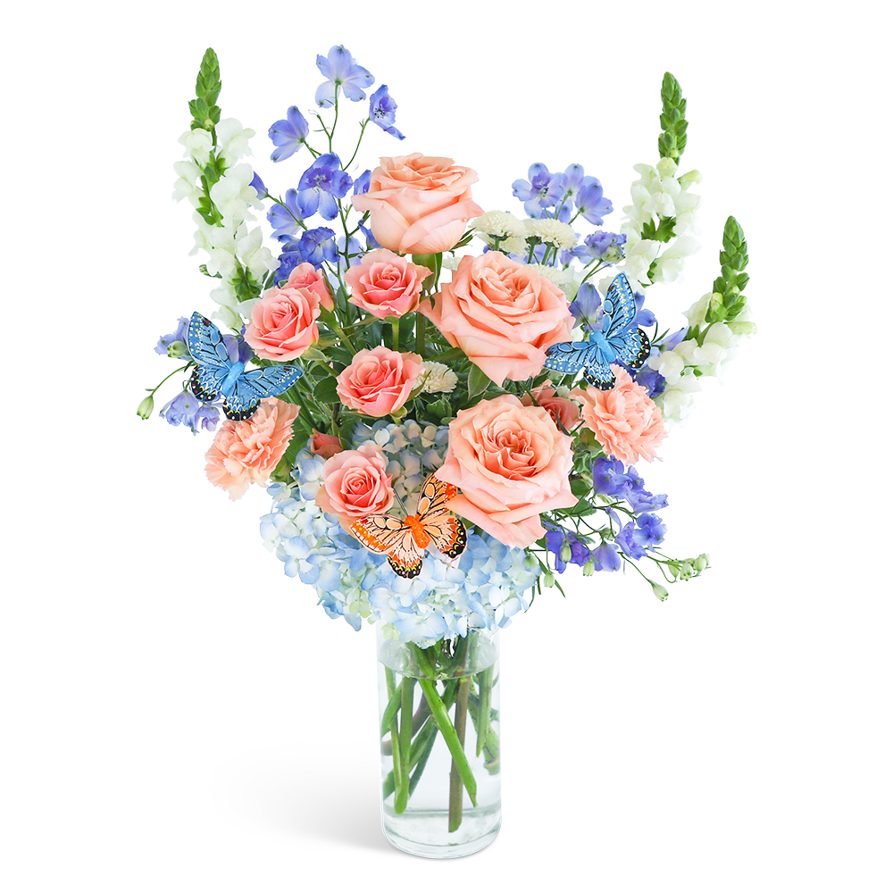 Peach roses and blue flowers in a clear glass vase with butterfly picks