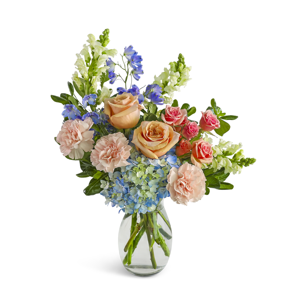 Peach roses, pink carnations, blue hydrangeas, and delphinium in a clear glass vase