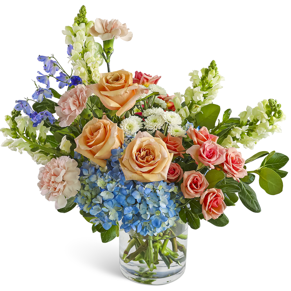 Mixed bouquet of peach roses, blue hydrangea, and assorted blooms in a clear glass vase