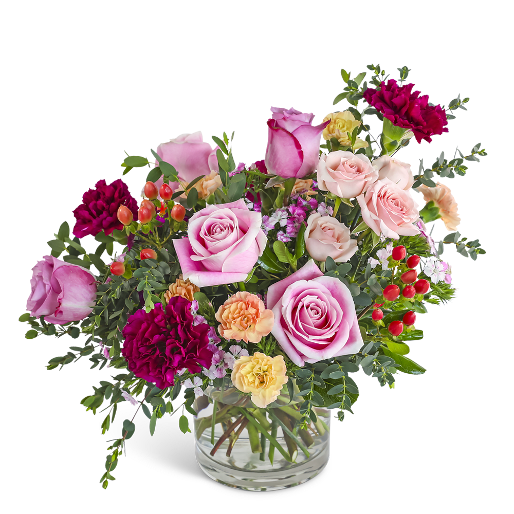 Short arrangement of pink roses, burgundy carnations, and peach blooms in a clear glass vase