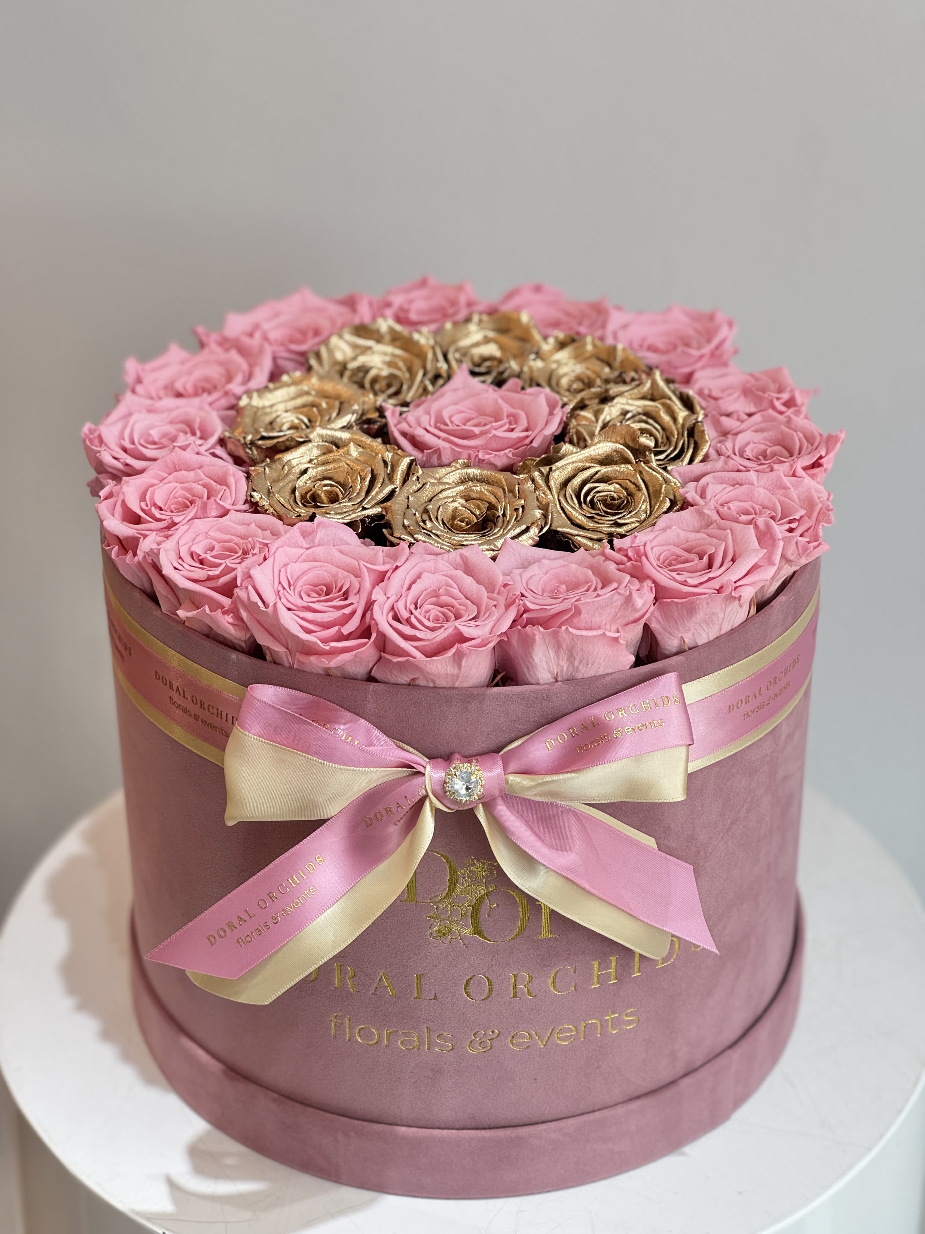 Pink and gold roses arranged in a round hat box with a ribbon bow