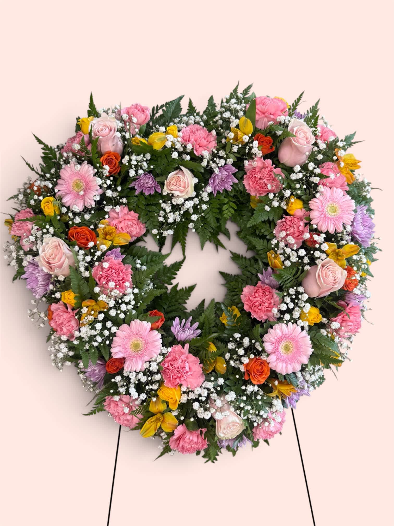 Heart-shaped floral wreath with pink, yellow, and white blooms on a stand