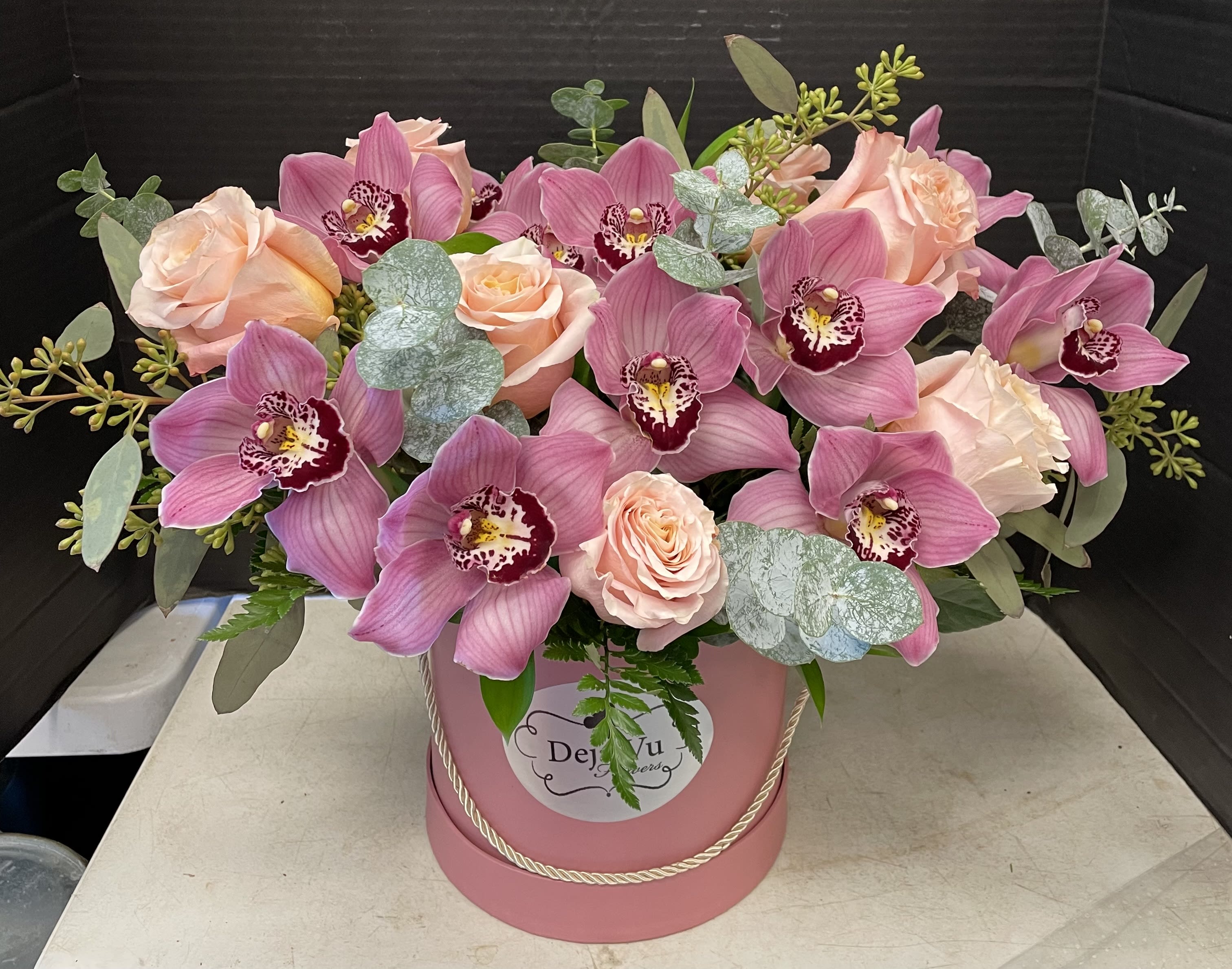 Pink orchids and peach roses arranged in a pink hatbox